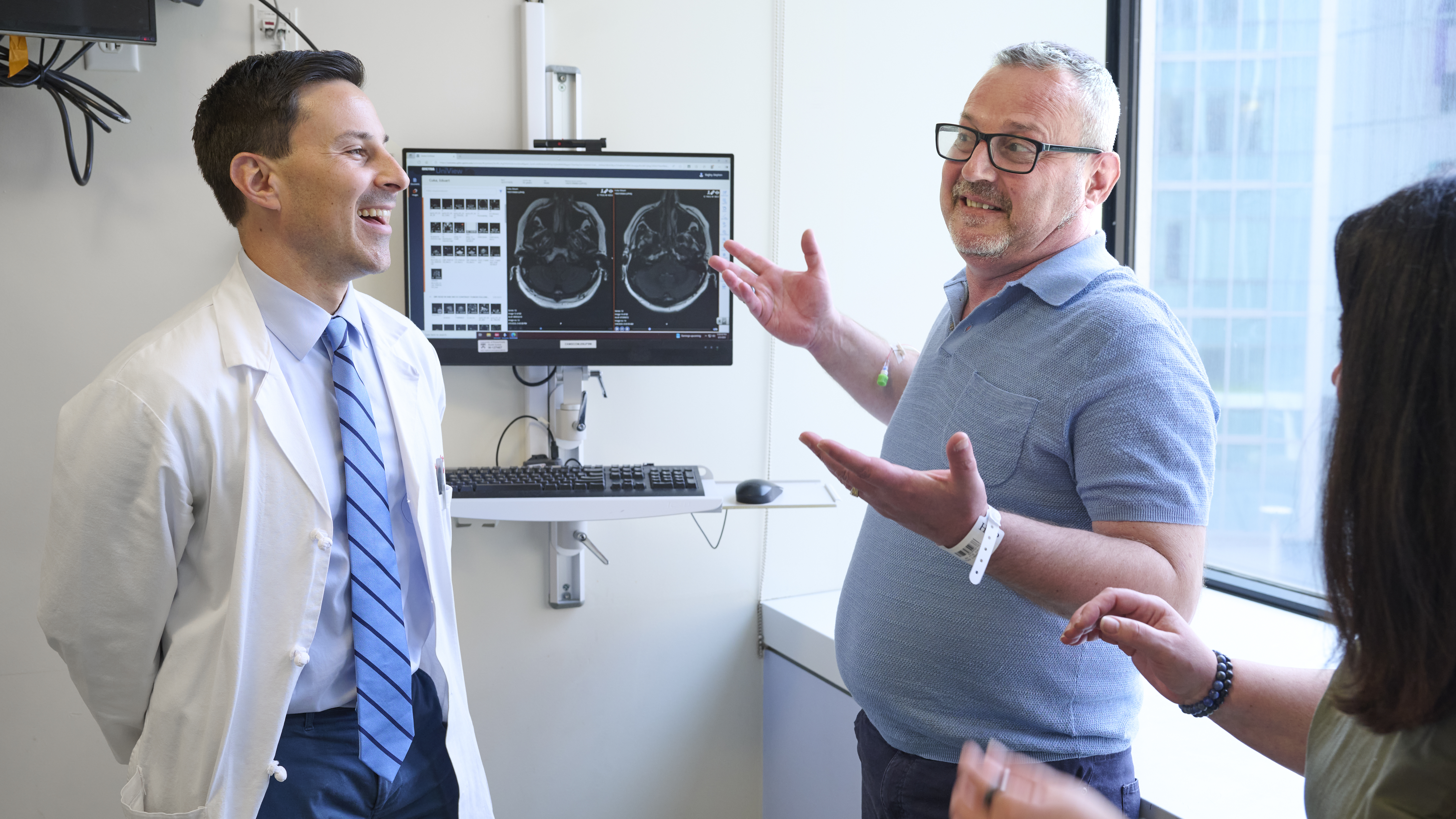 Stephen Bagley, MD, and Eduart Cuka both smile, as Eduart shrugs, with the profile of Juliana Cuka raising her arms in cheer 