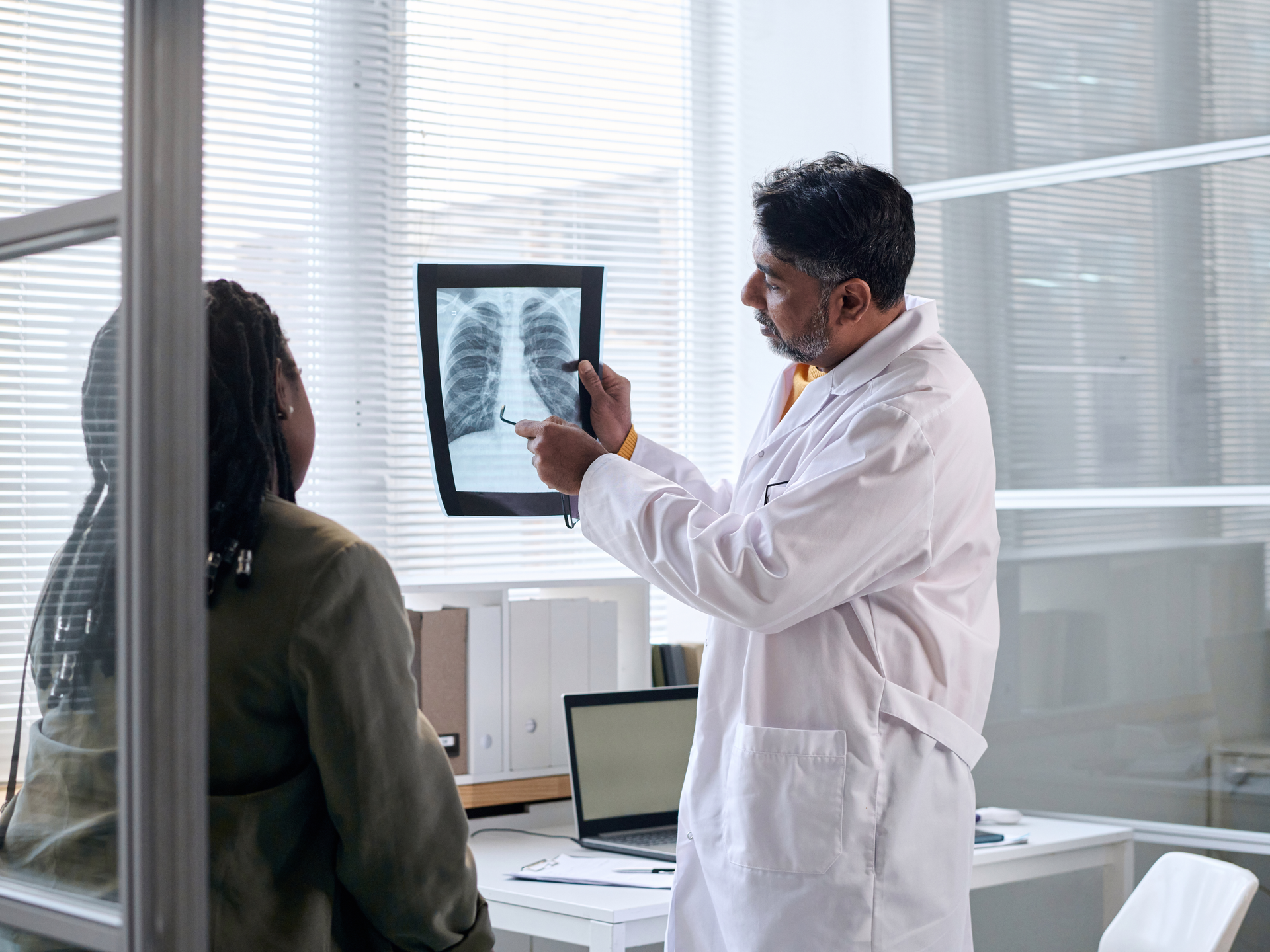 Side view portrait of senior doctor pointing at chest x ray while consulting patient in clinic