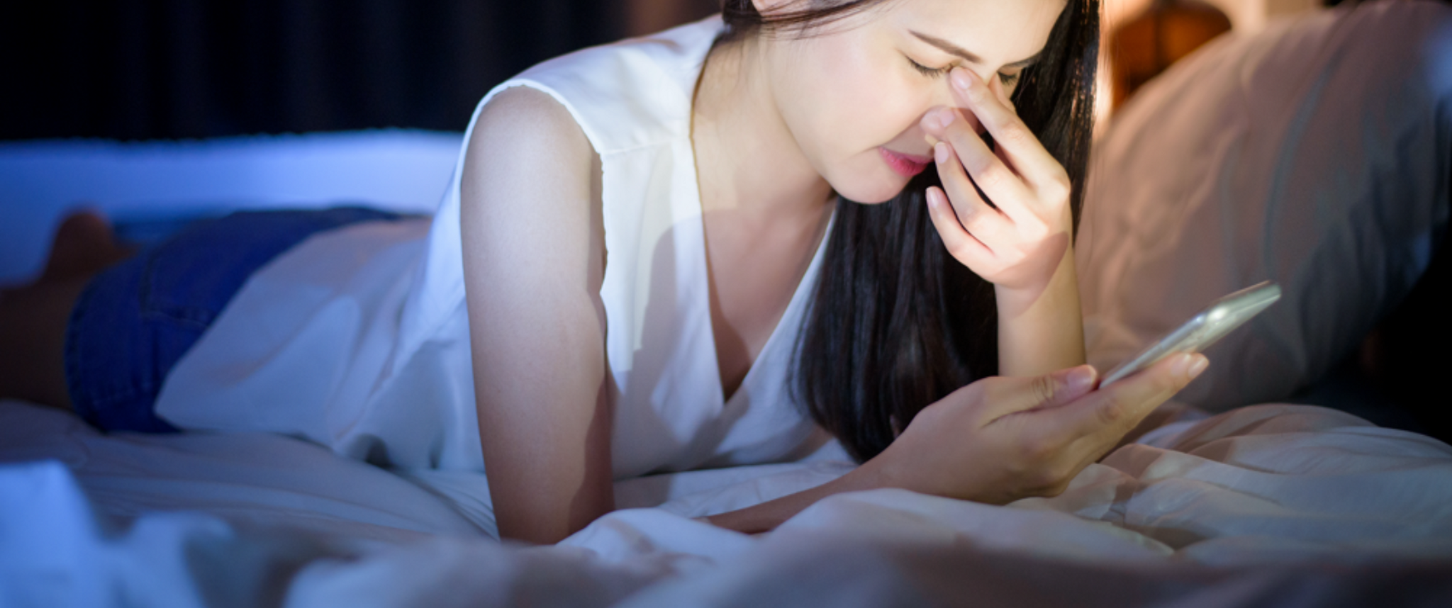 A woman with closed eyes holds her phone and pinches her nose and eyes
