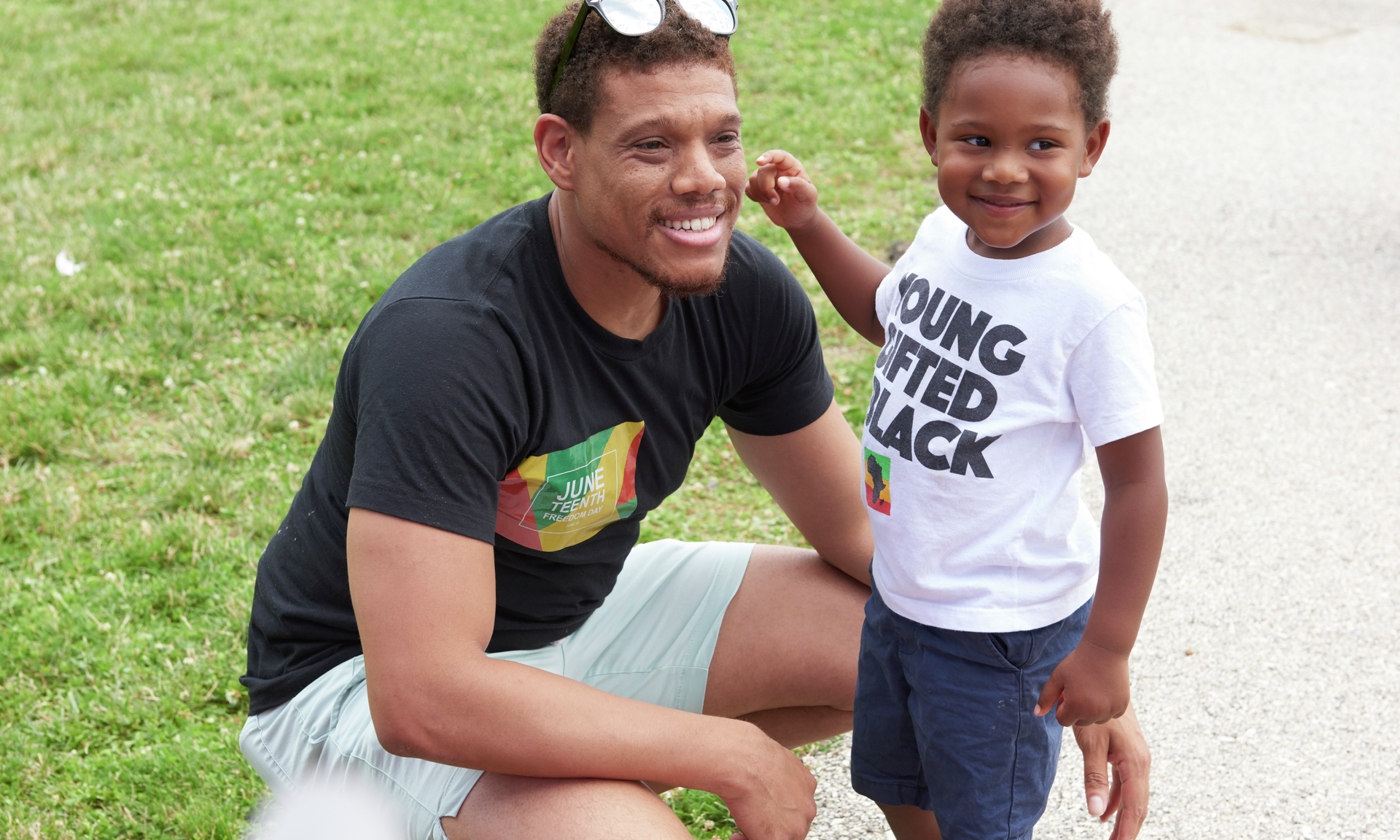 A young Black man kneels beside his smiling preschool-age son