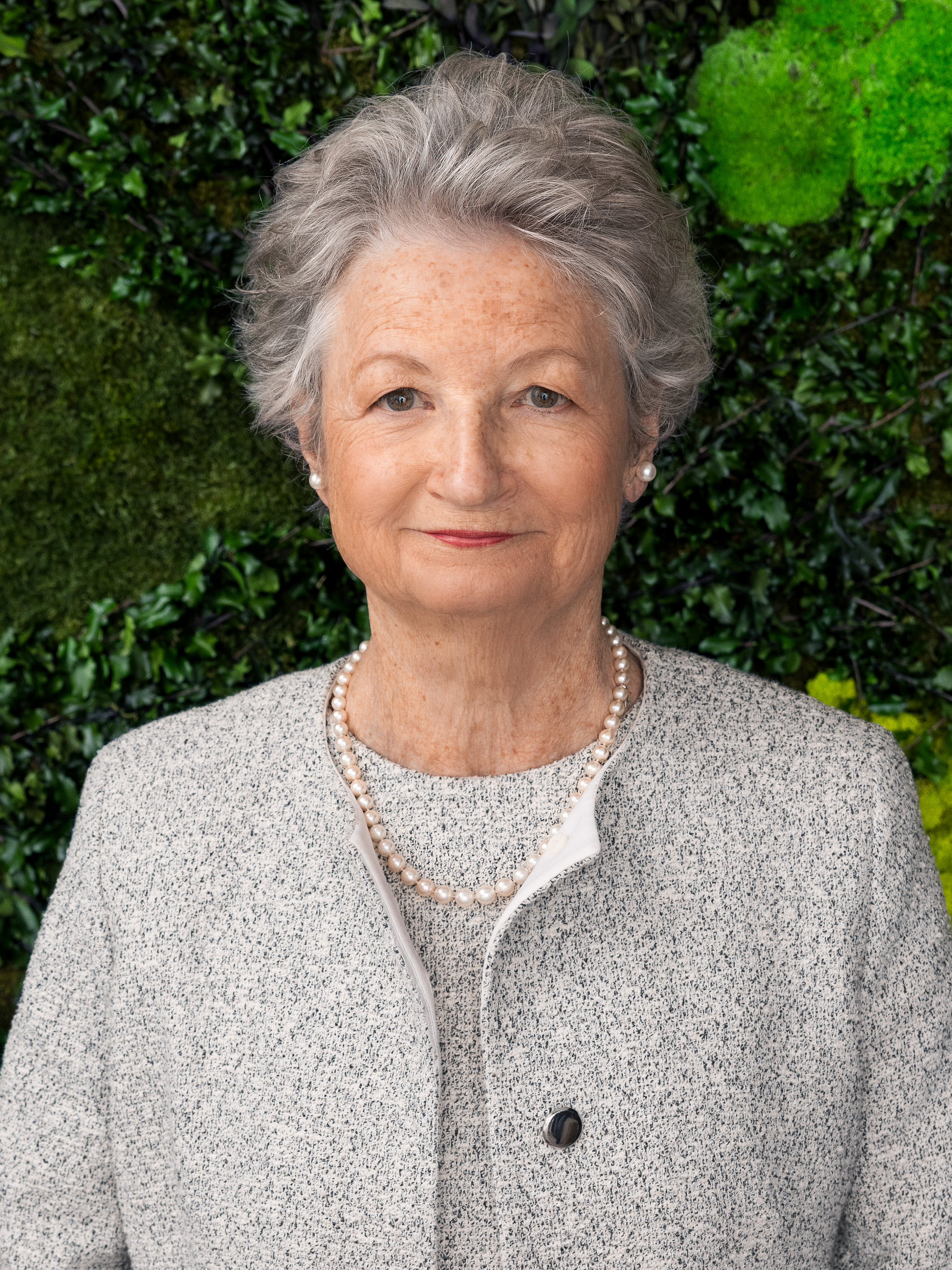 A portrait of Kathy High standing in front of a wall with greenery