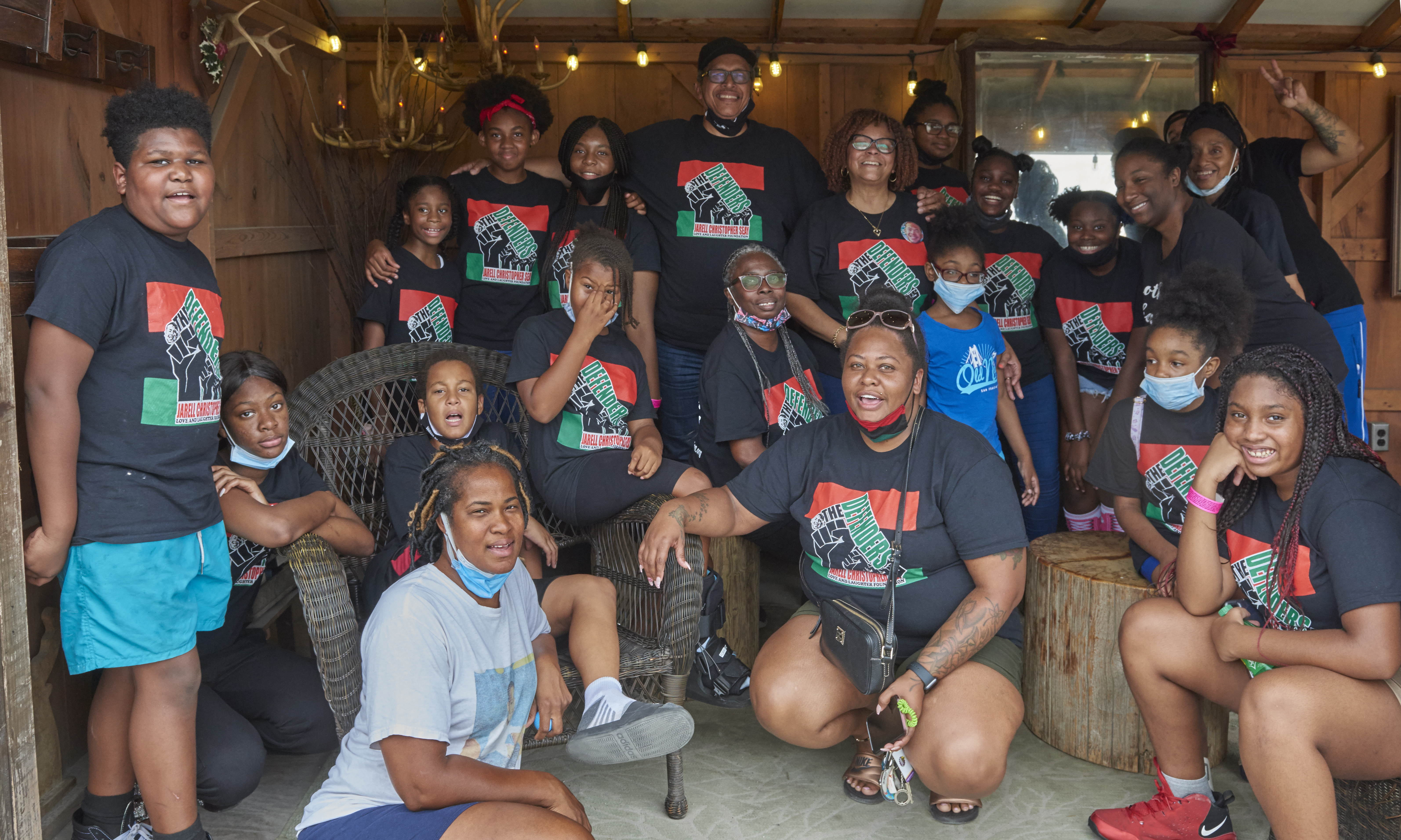 A group of adults and children mostly wearing "Defenders" T-shirts standing in a wooden structure