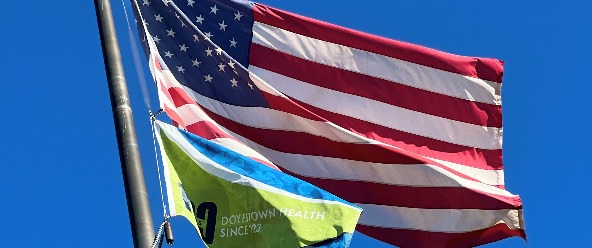 flagpole with a large American flag and smaller flag that says Doylestown Health Since 1923