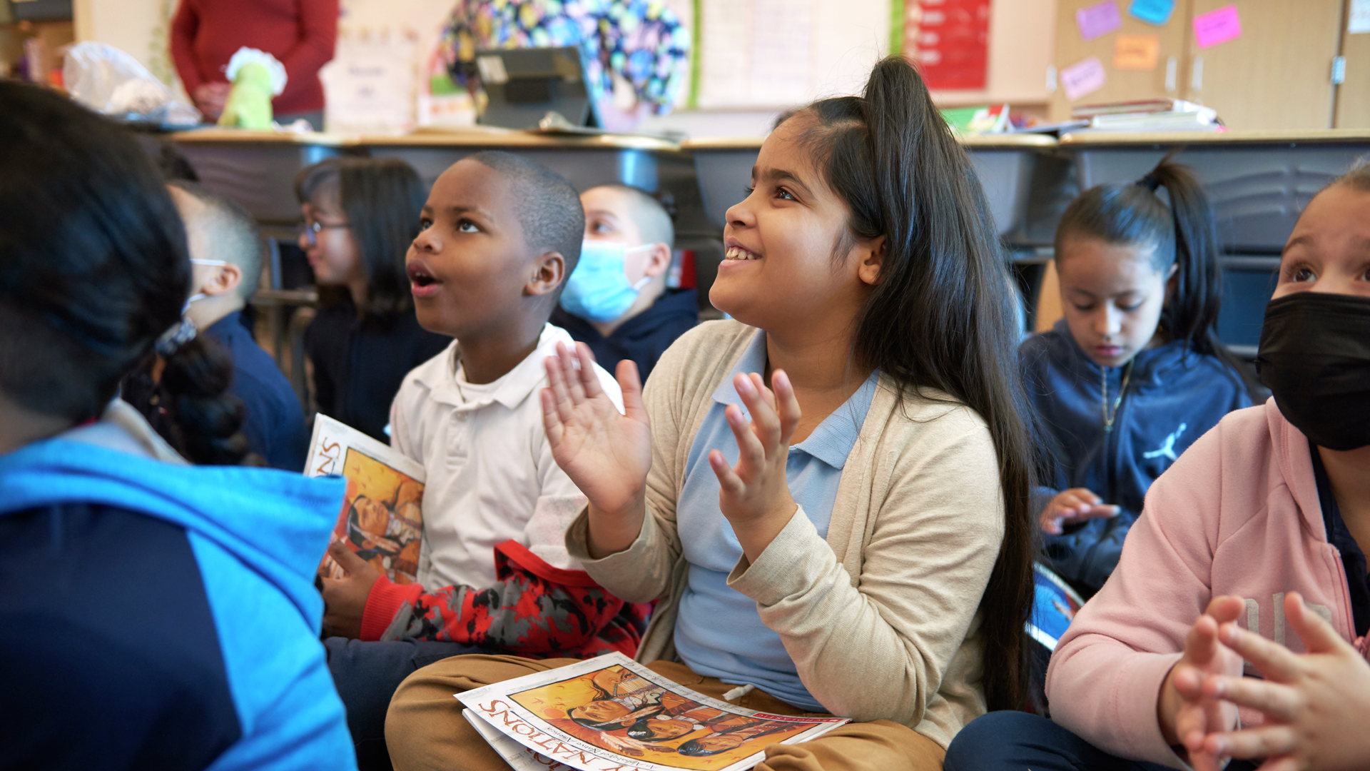 Young kids sit in a group on the floor with books in their laps and rapt expressions
