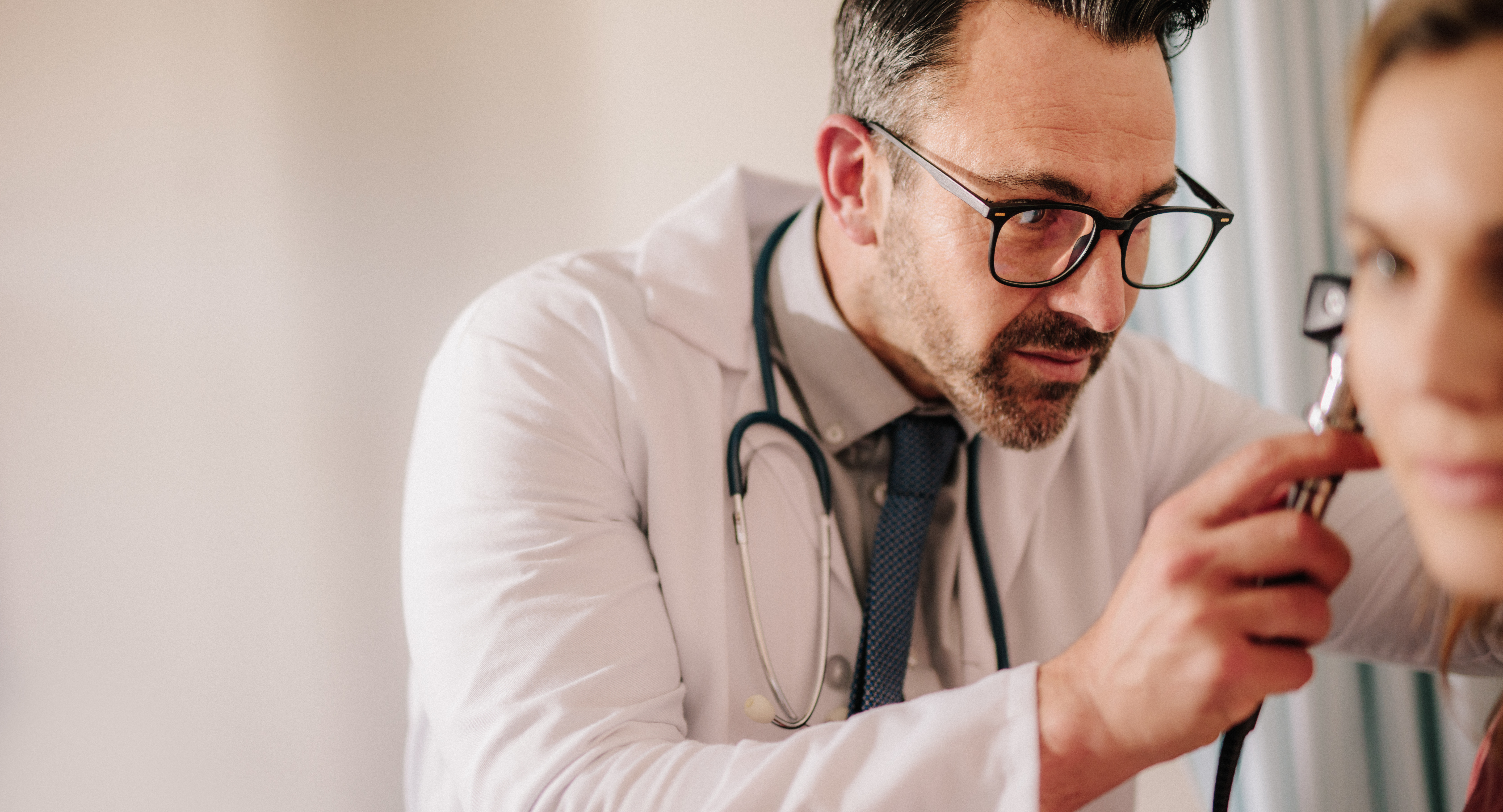 Male doctor looking at female patient's ear through otoscope