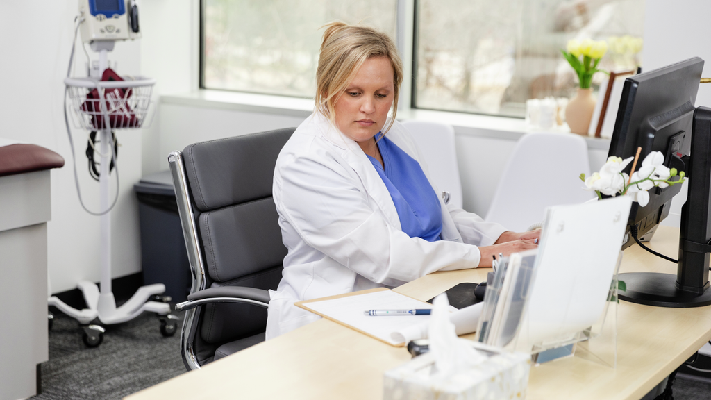 A doctor types on a computer at her desk