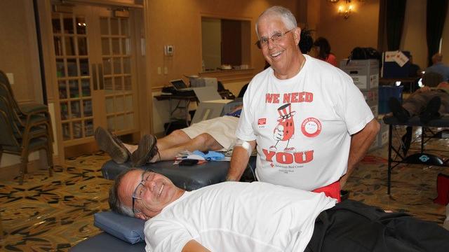 Marc A. Satalof, wearing a Red Cross T-shirt, stands beside a man lying on a cot at a blood drive Satalof chaired.
