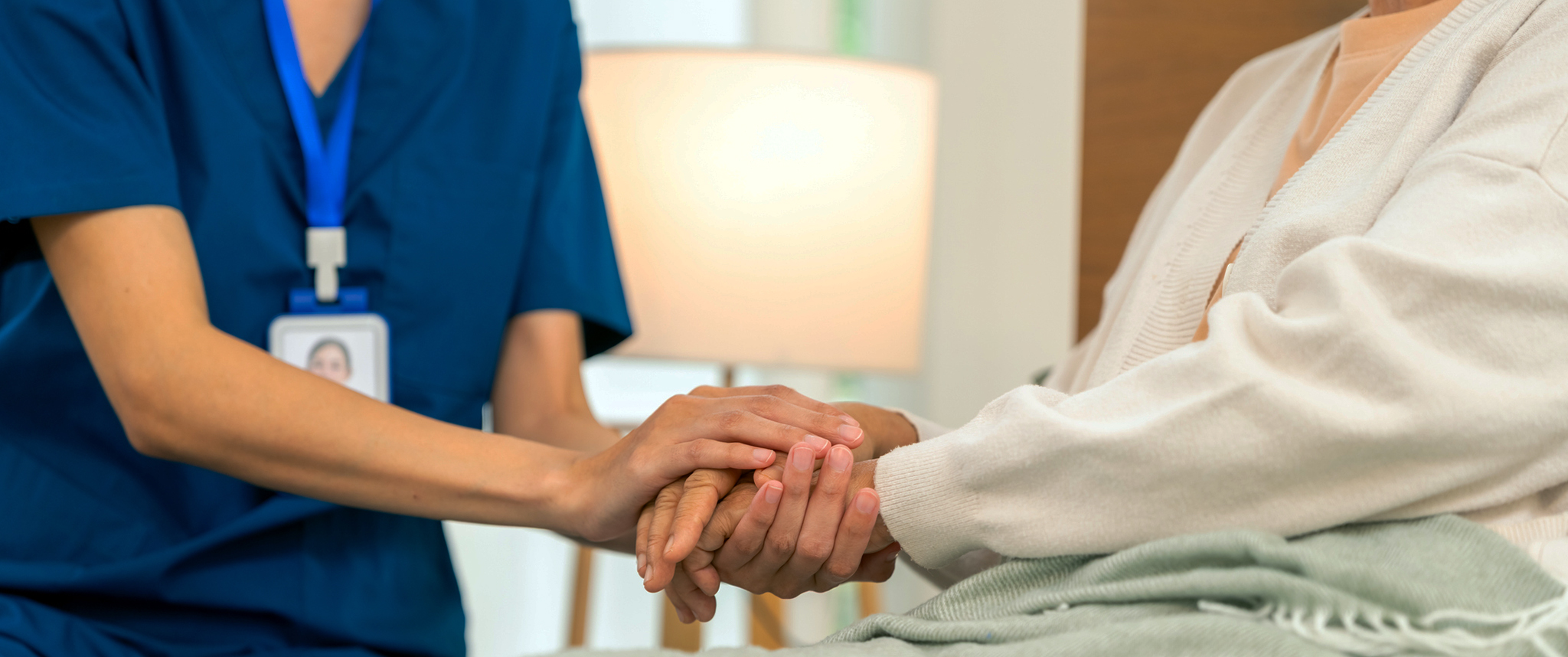 A nurse comforts an older woman patient at her hospital bed.