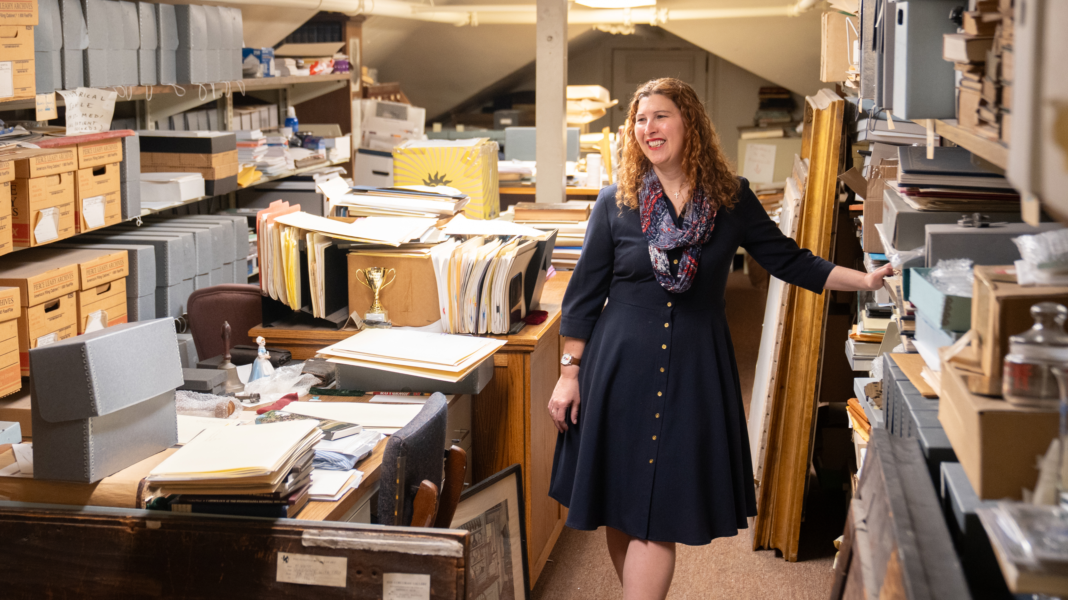 Stacey Peeples standing in her office, looking at shelves of books and artifacts 