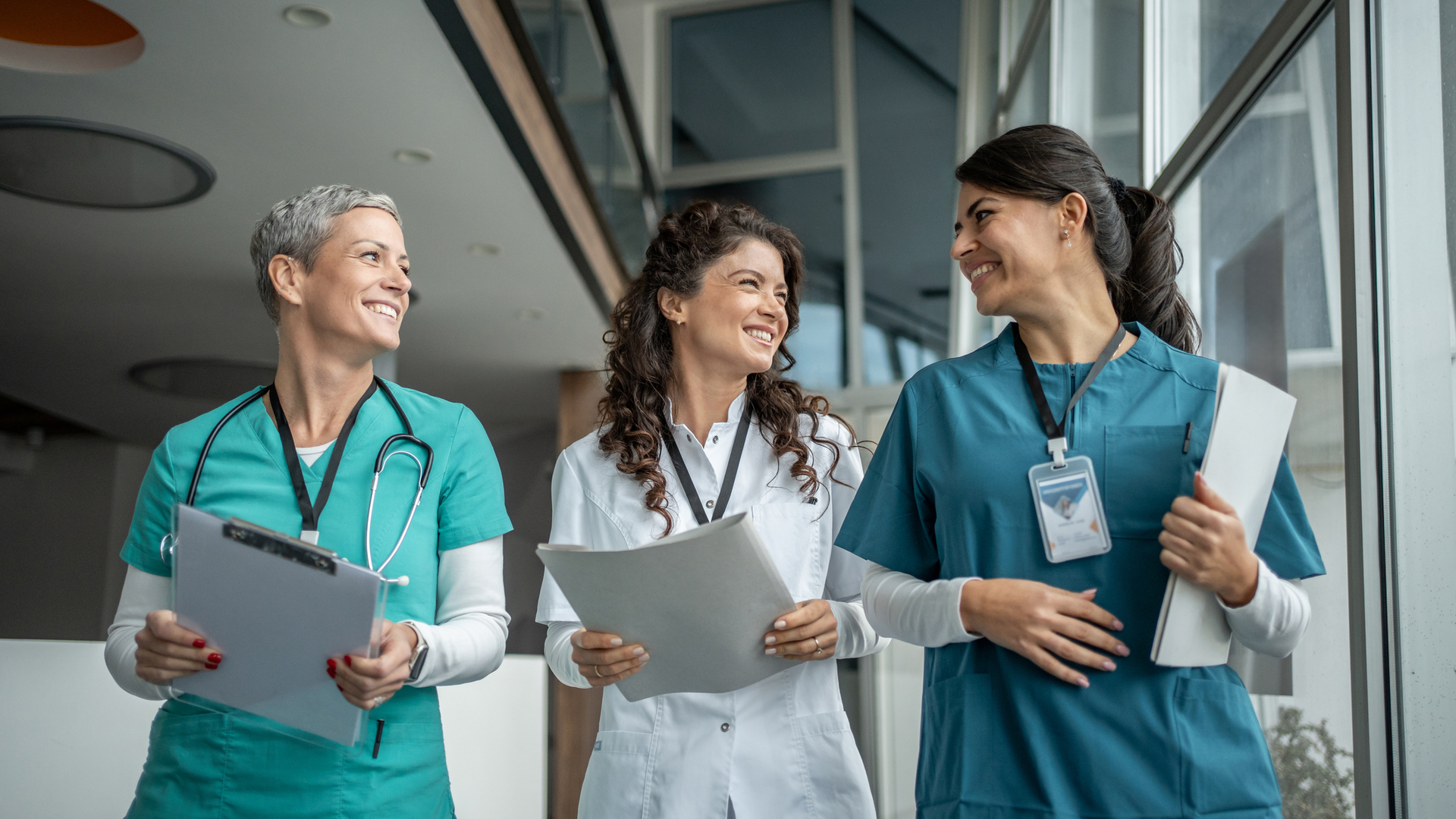 Three diverse female medical professionals are walking and smiling, engaged in conversation.