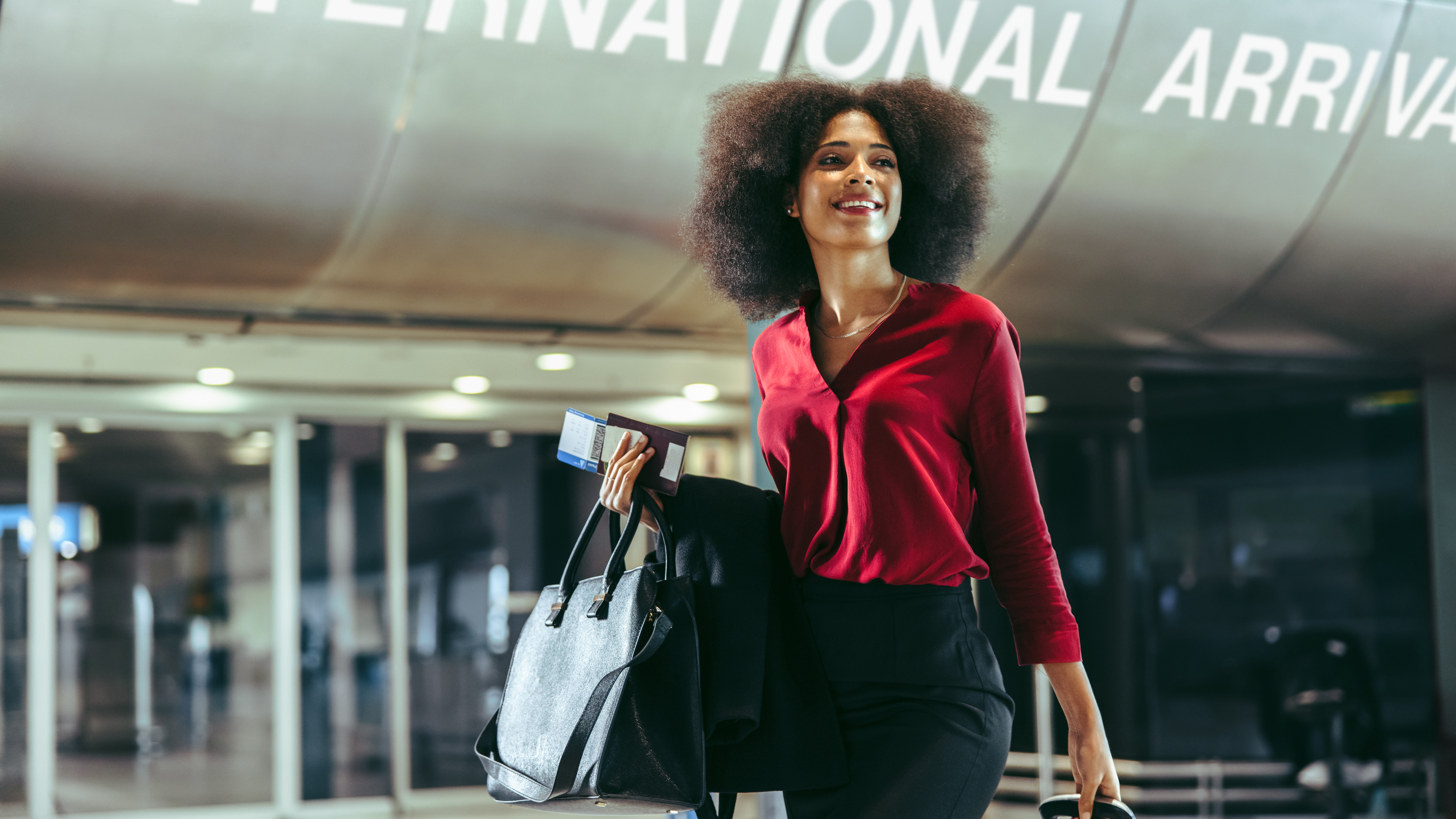 A woman standing with her suitcase and purse in front of a building reading 'International Airport'.