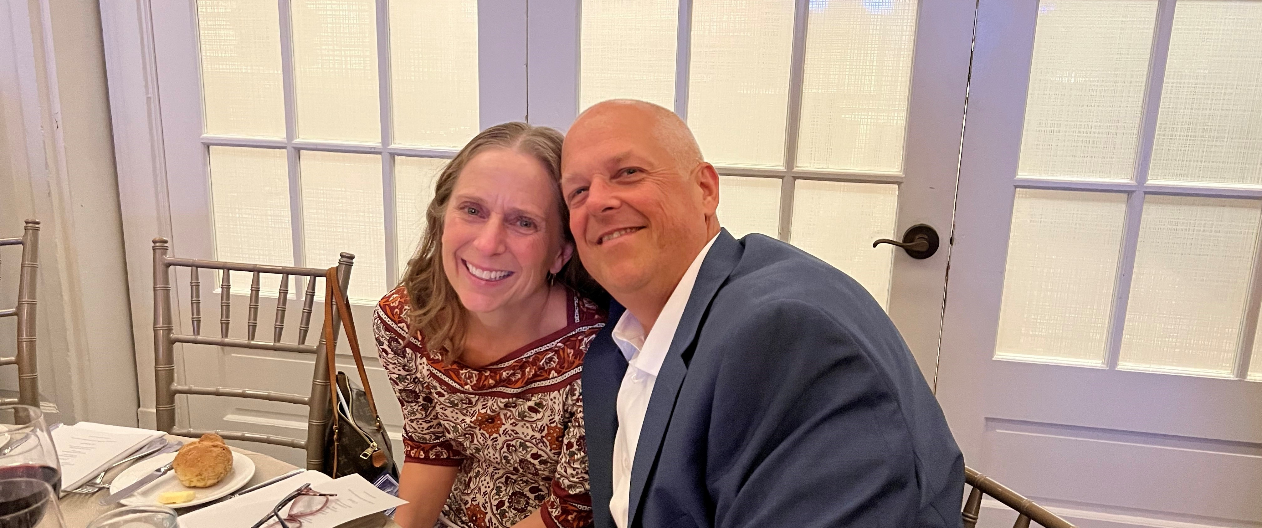 Joanie smiles with her husband at a dinner table
