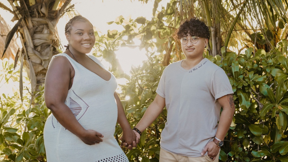 Jennifer Anderson and Mick Masaba hold hands in front of palm trees and other plants