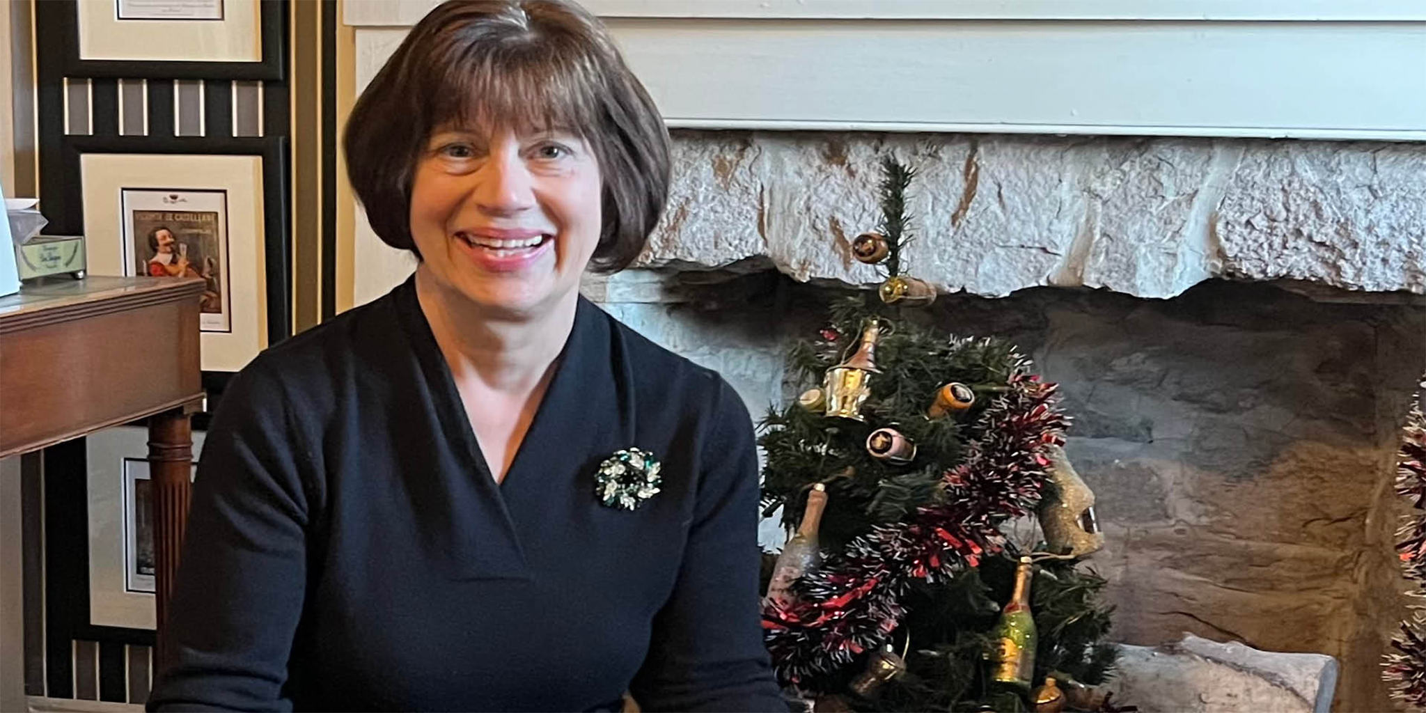 Nancy Holland smiles in front of a miniature decorated Christmas tree at home