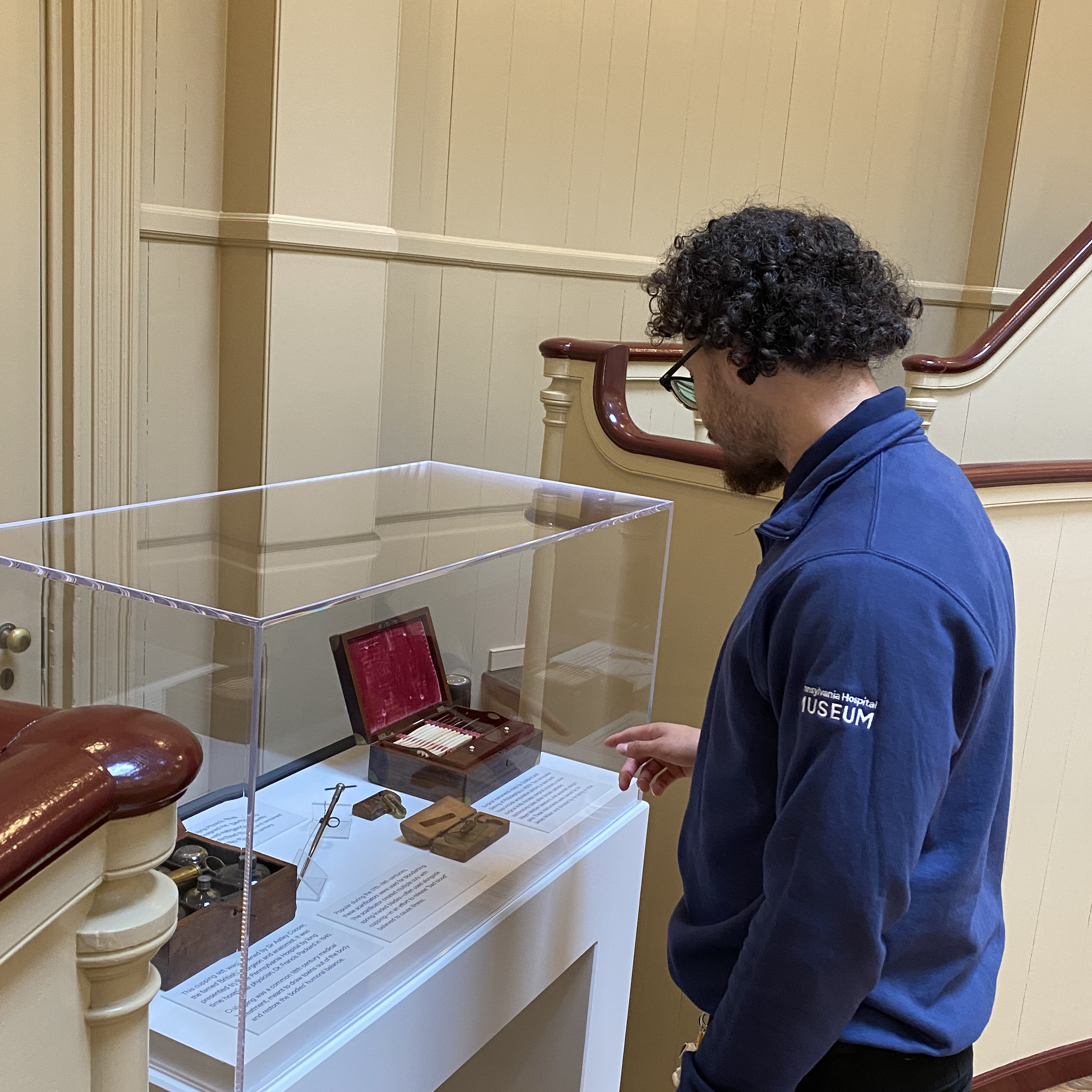 Isaiah Reyes, a welcome desk ambassador, looking and pointing at early surgical tools in the Pennsylvania Hospital Museum