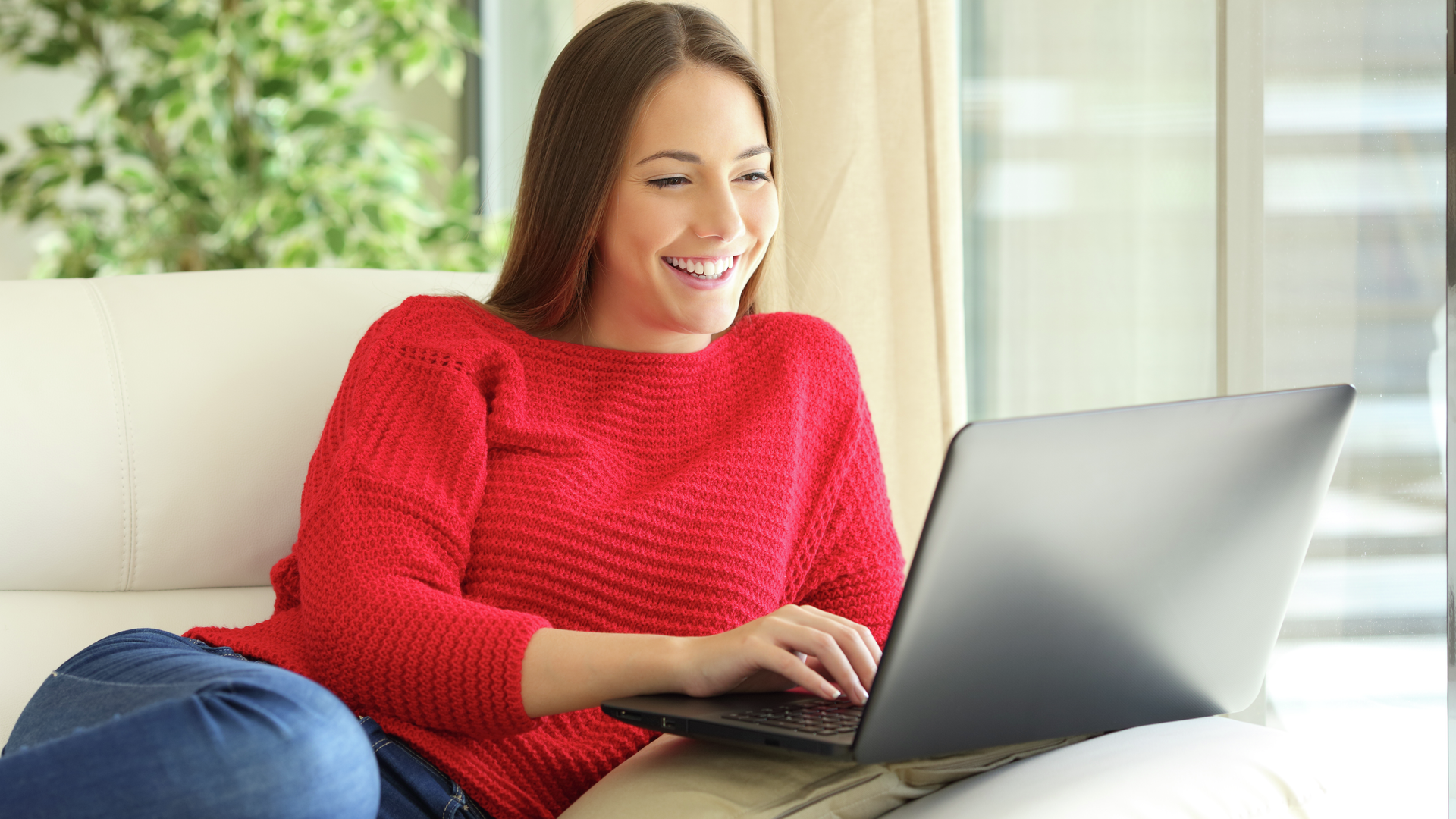 Happy woman wearing a red sweater using a laptop on line sitting on a sofa in the living room