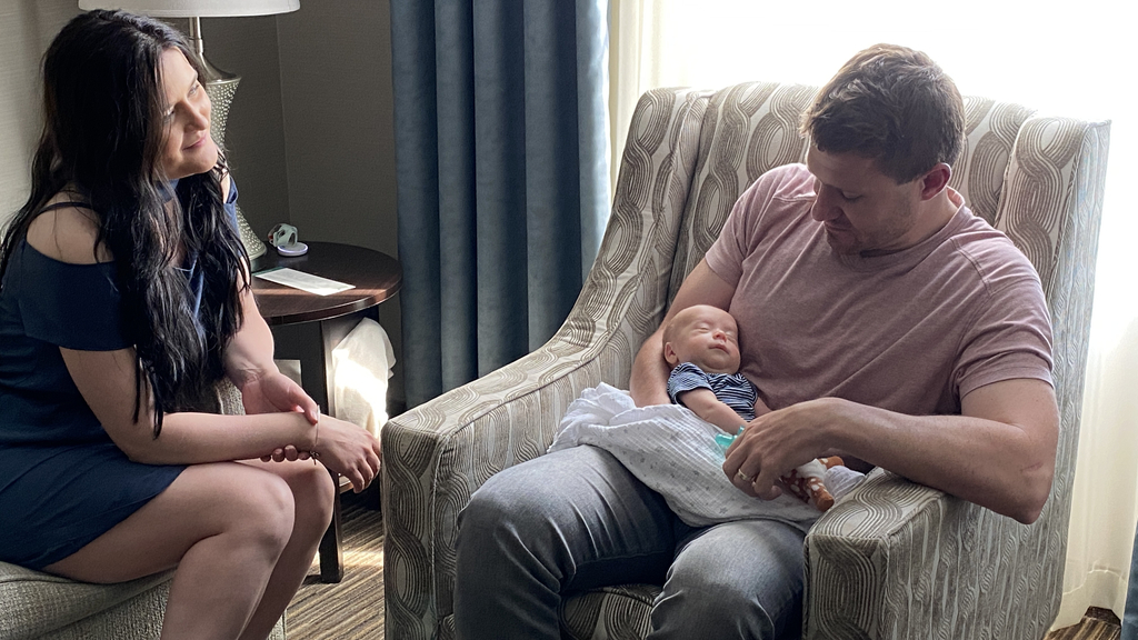 Jake Jovanovich holds baby Telden while sitting in an armchair and talking with Chelsea