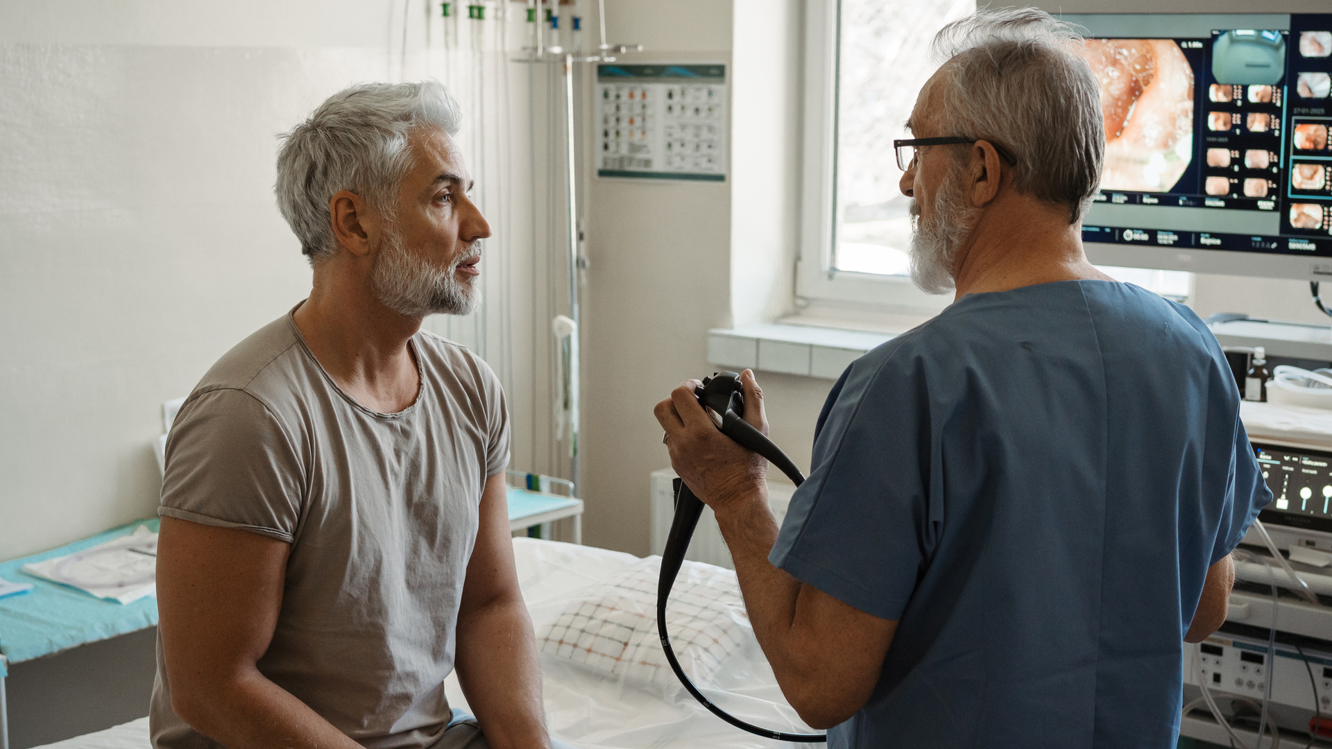 Doctor explaining colonoscopy results to patient using monitor images on screen.