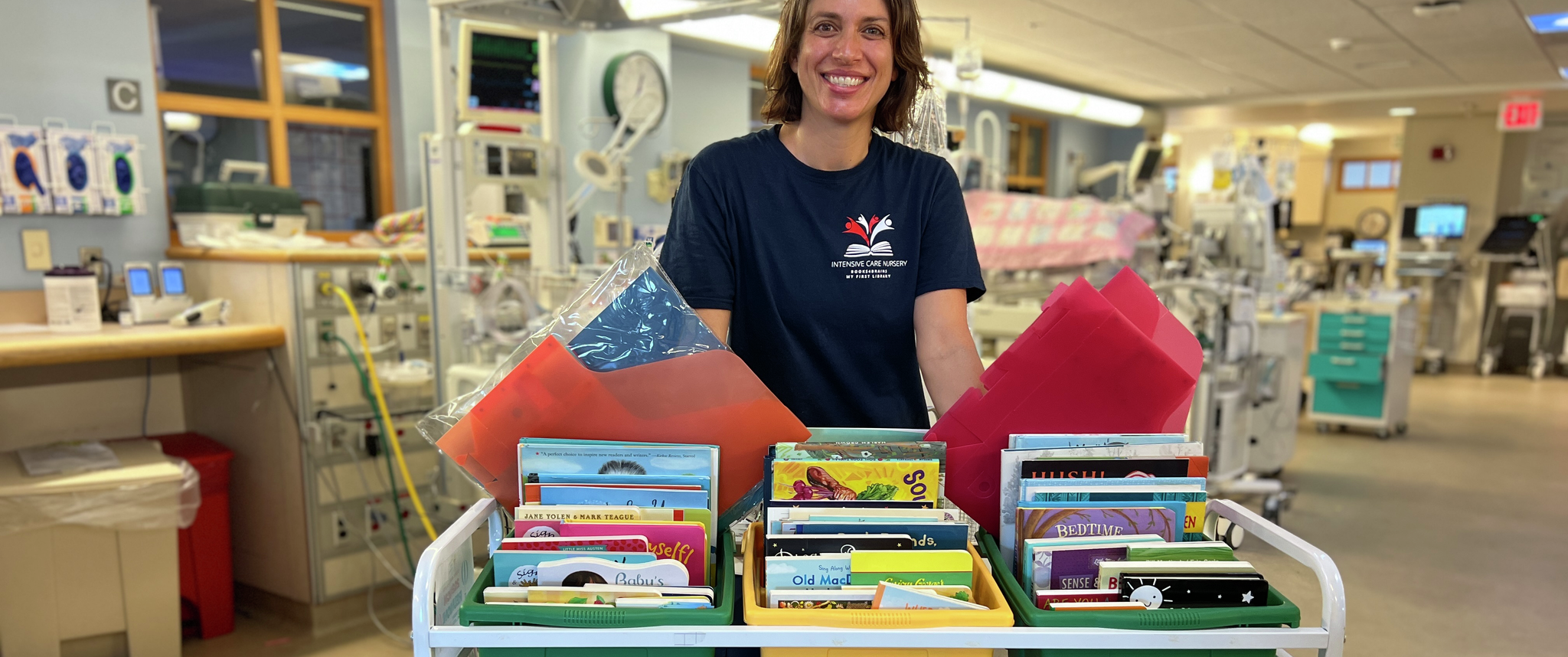 Whitney Zachritz, MSN, RN, CPNP-BC, a nursing professional development specialist at the Hospital of the University of Pennsylvania, stands behind a cart filled with books.
