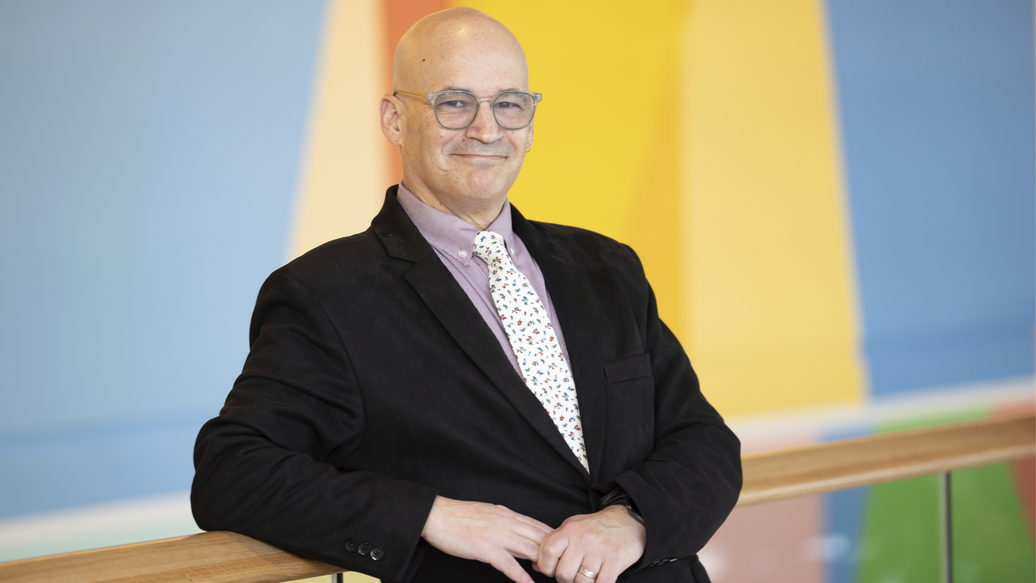 Enrique Schisterman leans against a railing with a colorful mural behind him