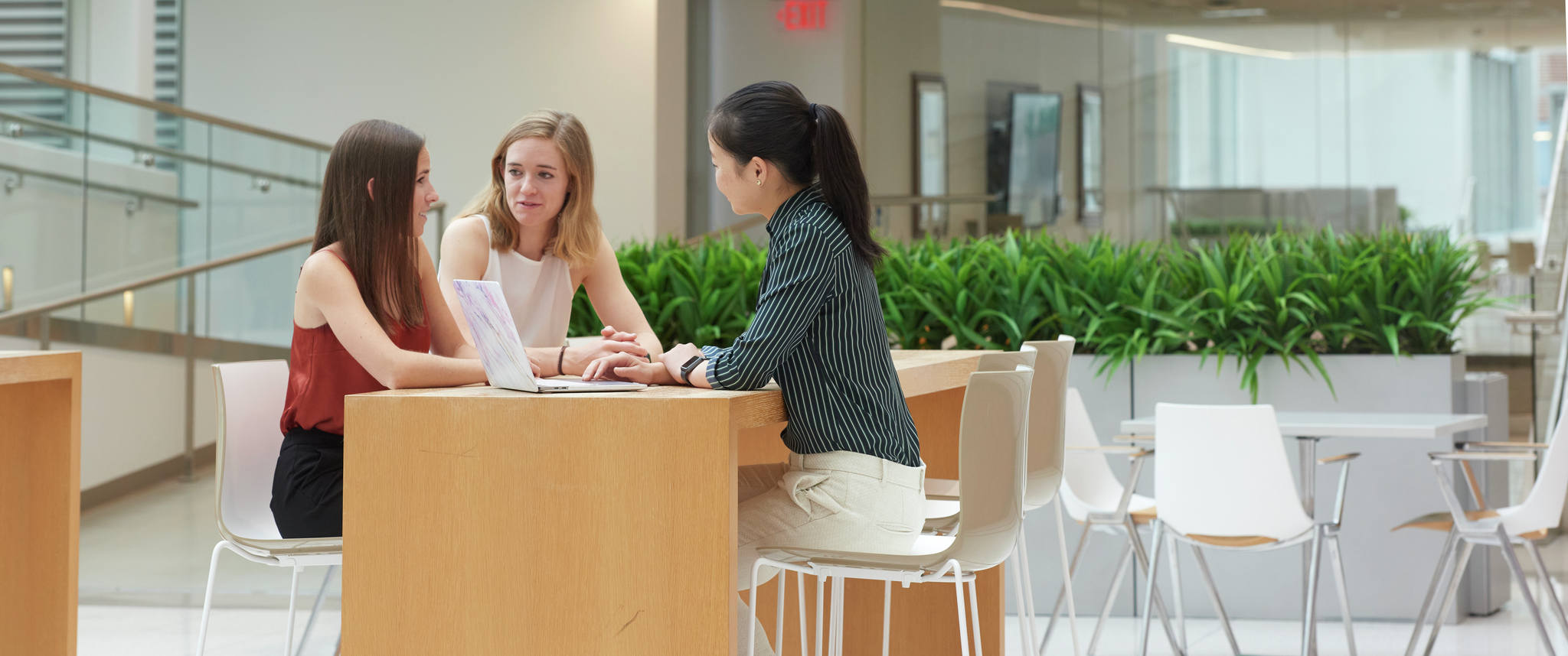 Three Penn medical students in the Jordan Medical Education Center atrium sit at a high-top table appearing to discuss information on a laptop between them