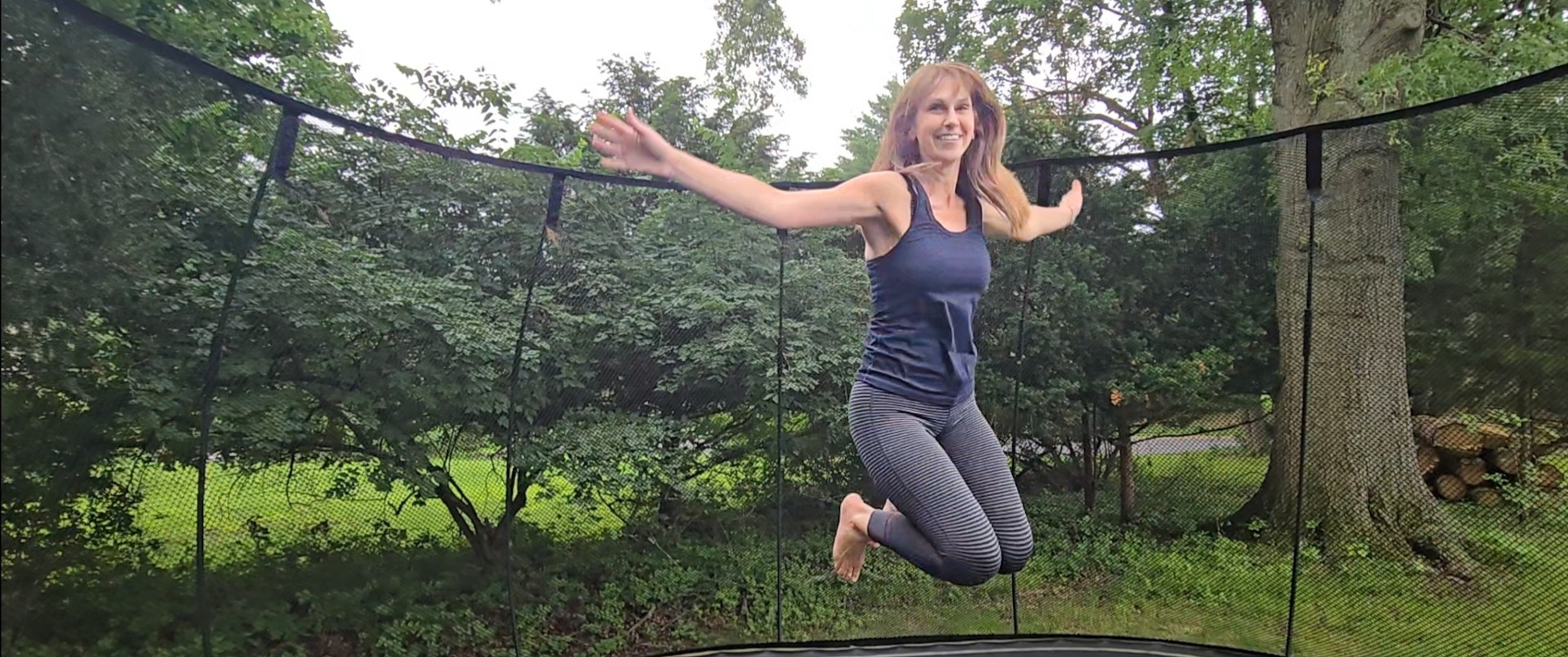 Pam Cobb jumps on a trampoline in a green backyard