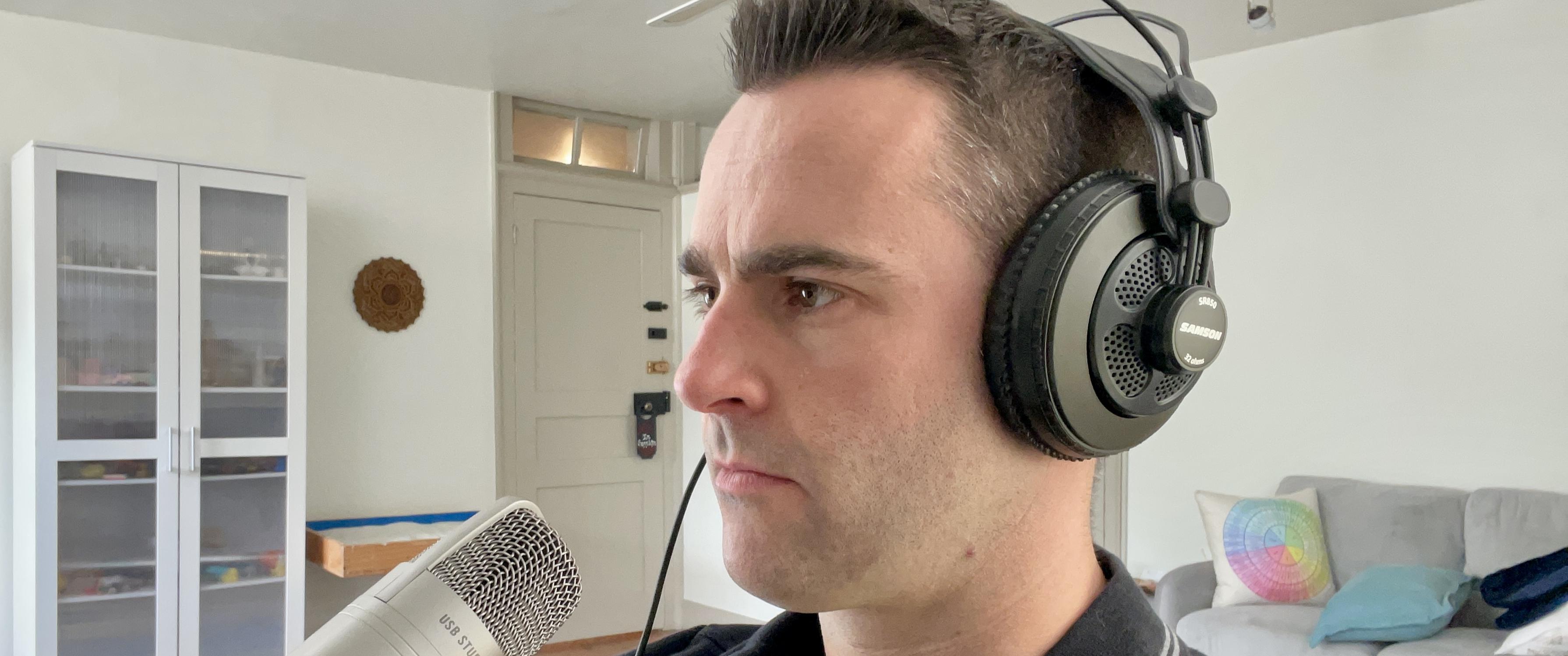 Andy Dean, in a living room, wearing over-the-ear headphones and facing a microphone