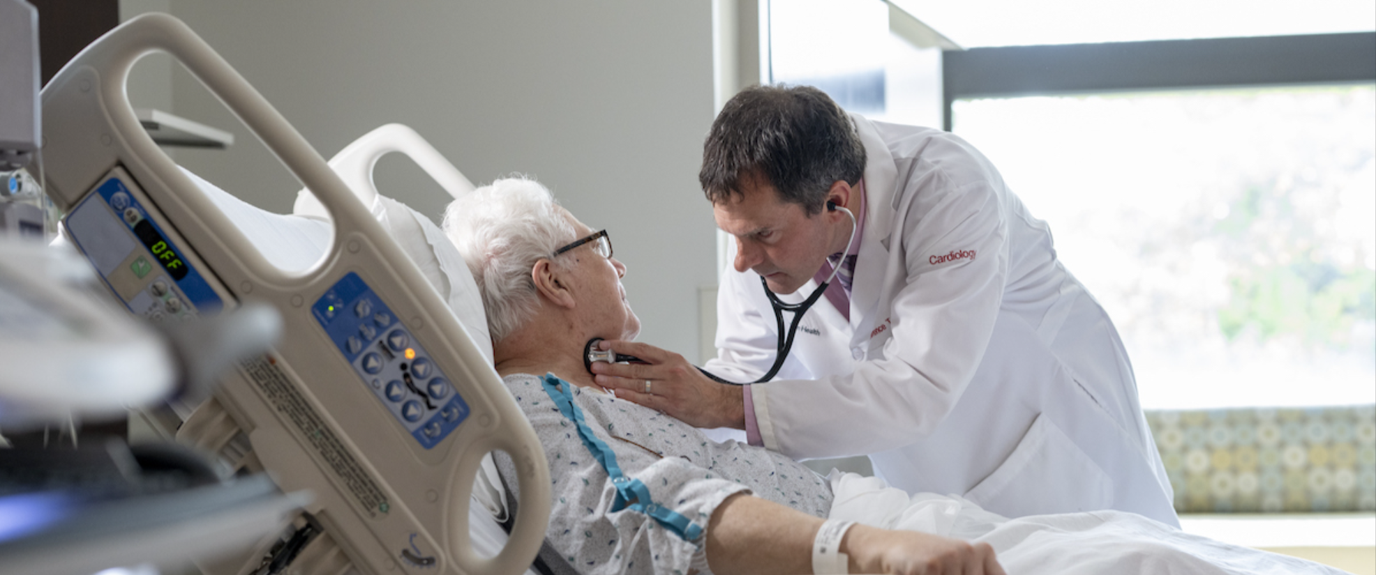 A cardiologist holds a stethoscope to an elderly man’s neck to check for abnormal blood flow in the carotid artery.