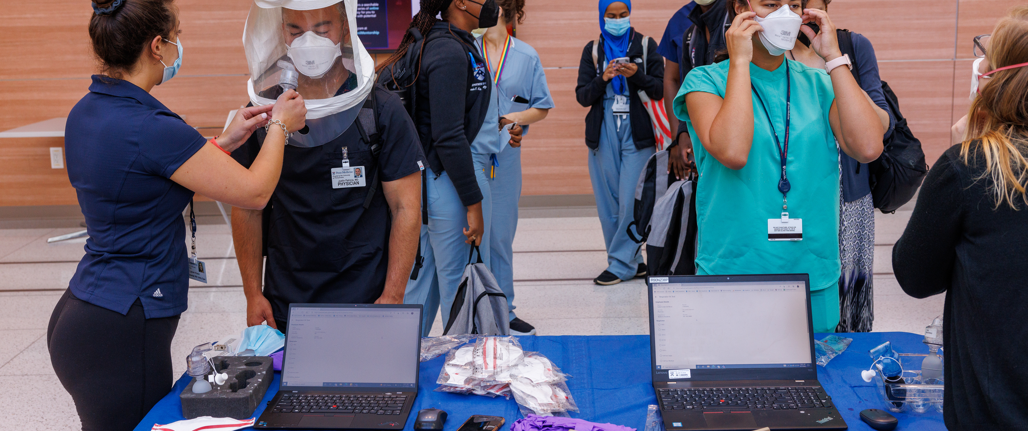 Young doctors of various races and ethnicities line up to be fitted for personal protective equipment