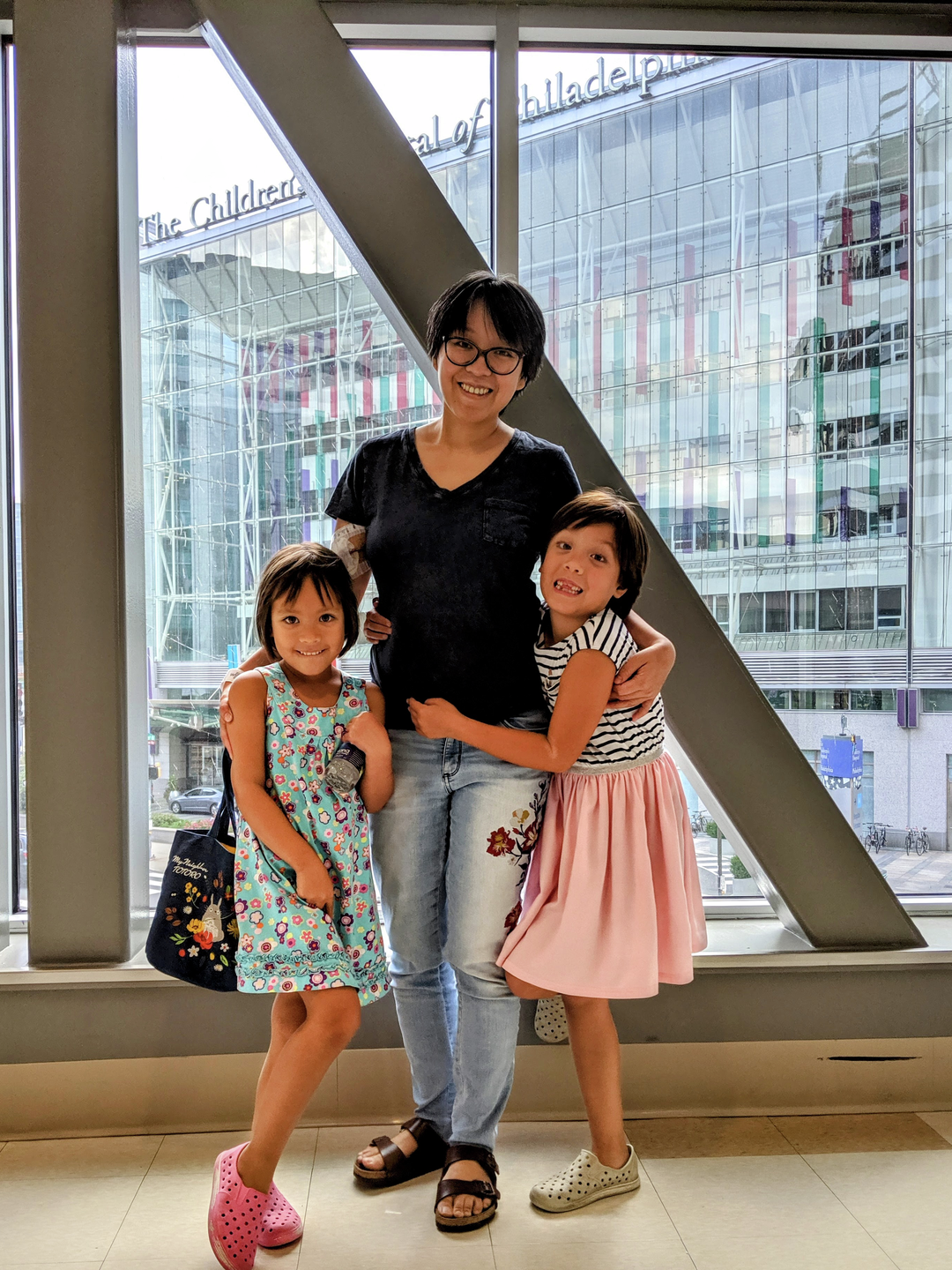 Becky Yu stands, smiling, with arms around her two daughters