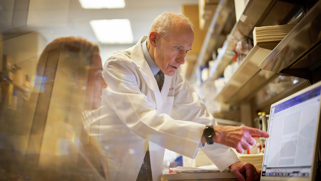 Carl June pointing to screen and talking to female researcher in lab