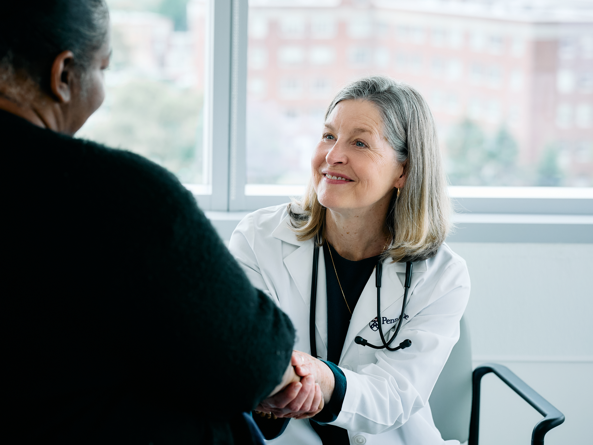 Doctor holding patients hand and smiling in exam room