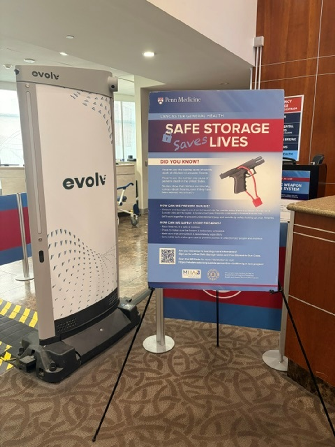 A poster that reads Safe Storage Saves Lives is on a stand next to an Evolv screening station at the entrance to Lancaster General Hospital.