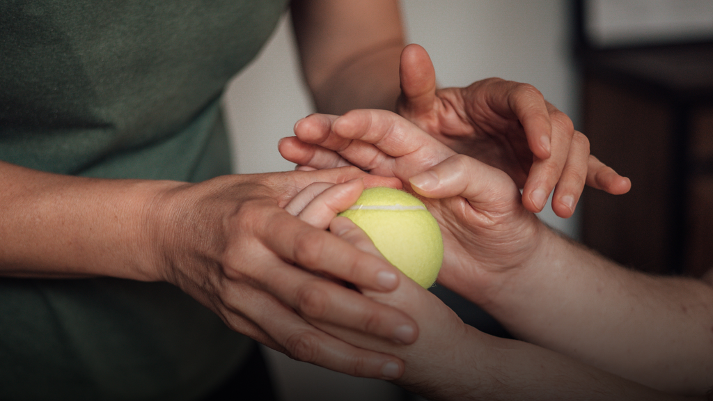 Luka Krizanac’s hands holding a tennis ball, while his physical therapist is holding his hands in hers
