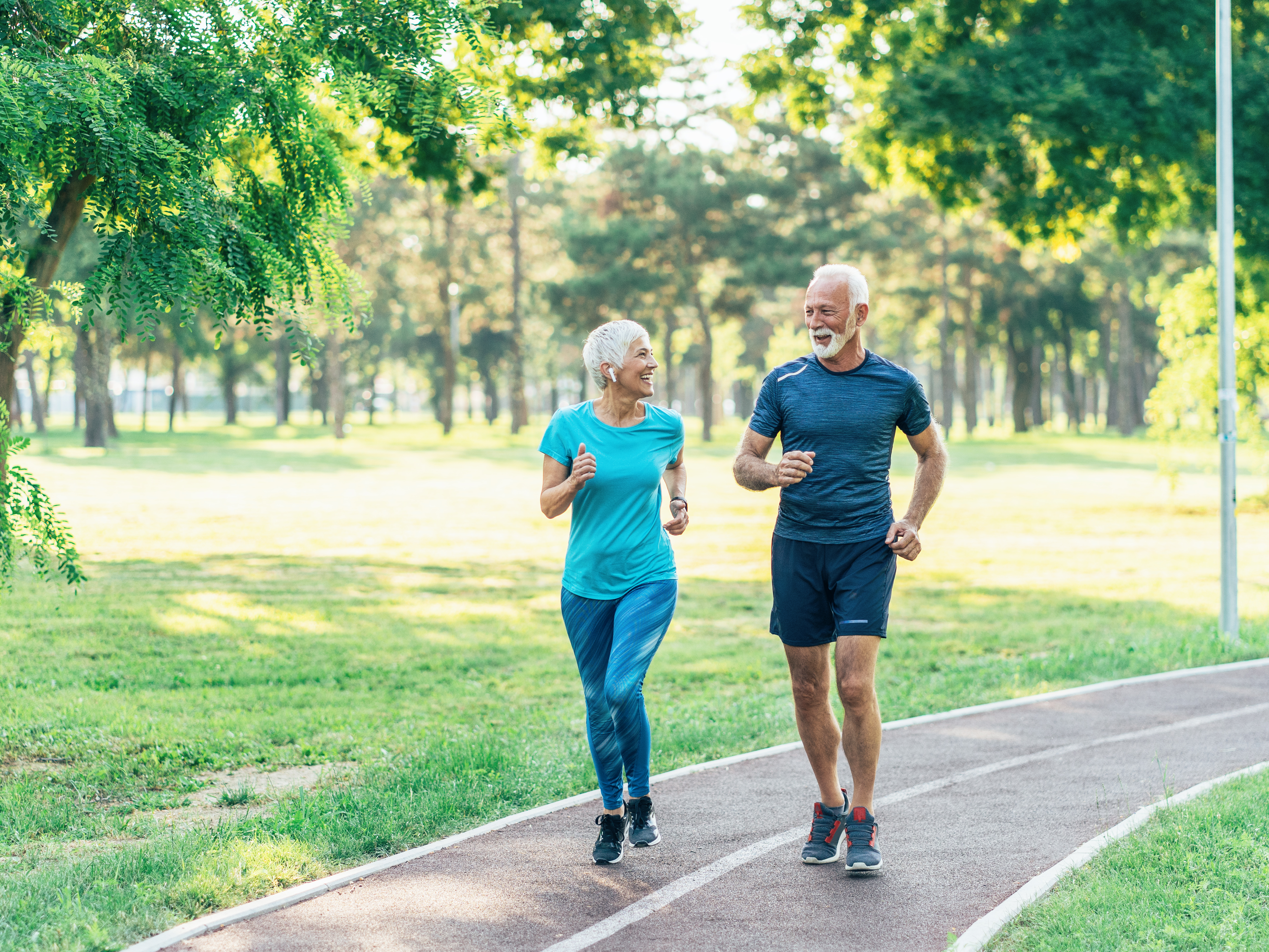 An elderly couple jogging outside, smiling at each other. 