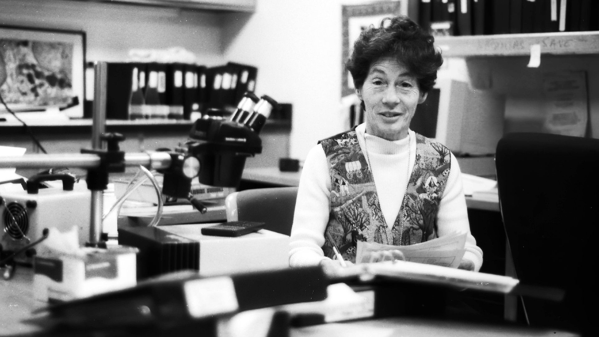 Black and white photo of Clara Franzini in middle age, at a desk with microscope and surrounded by binders
