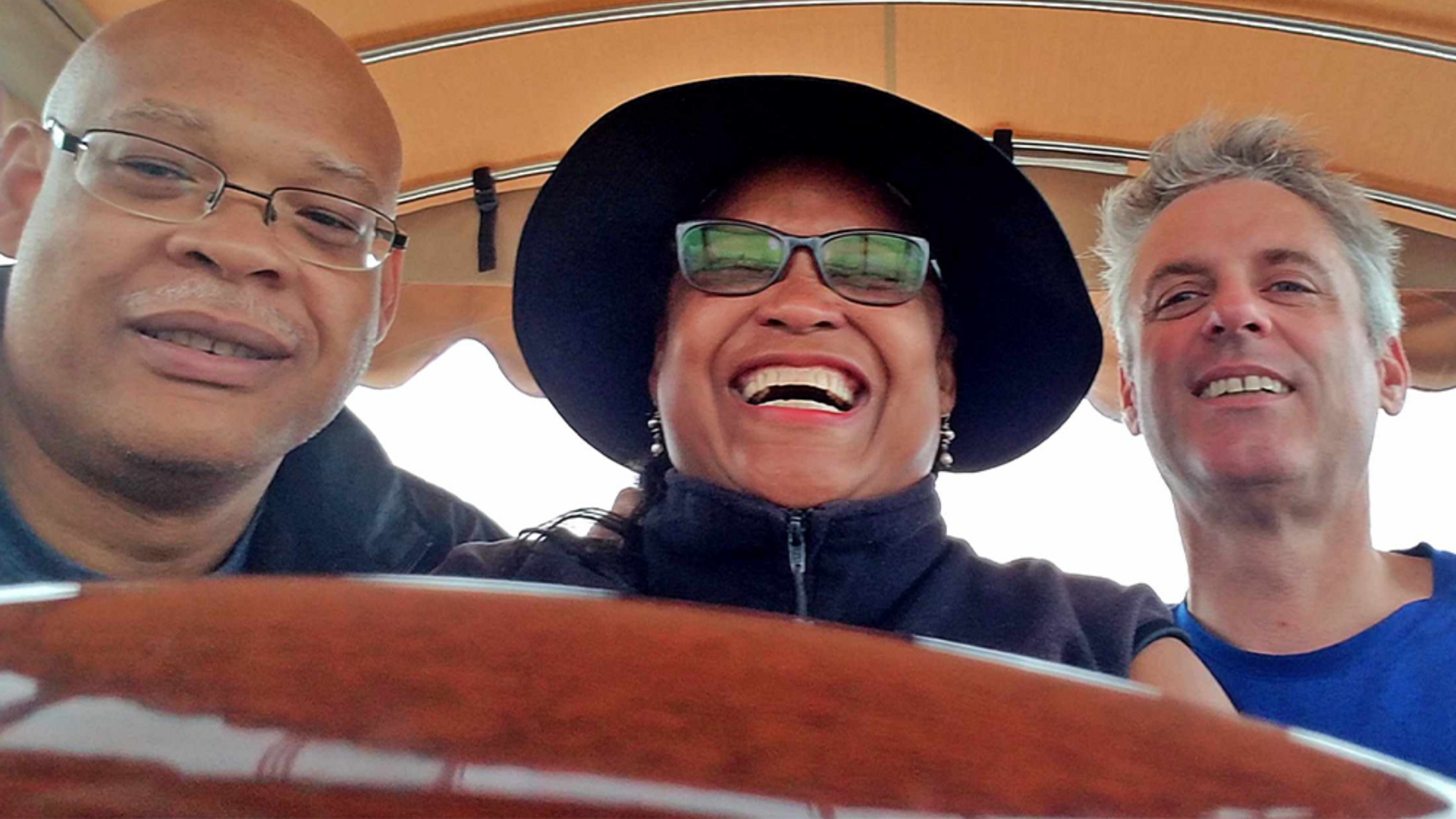 Frantz Dickerson, a bald Black man with glasses, next to his sister Nygra, smiling and wearing a hat and sunglasses, and her husband, David, also smiling