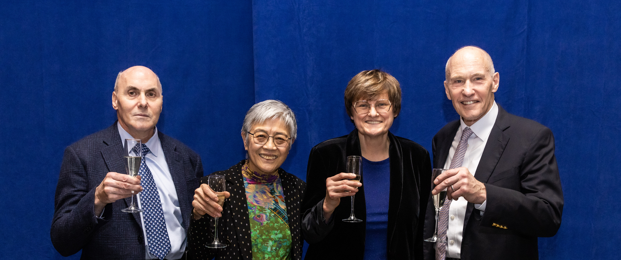 Drew Weissman, Virginia Lee, Katalin Kariko, and Carl June stand in front of a blue backdrop holding up champagne glasses
