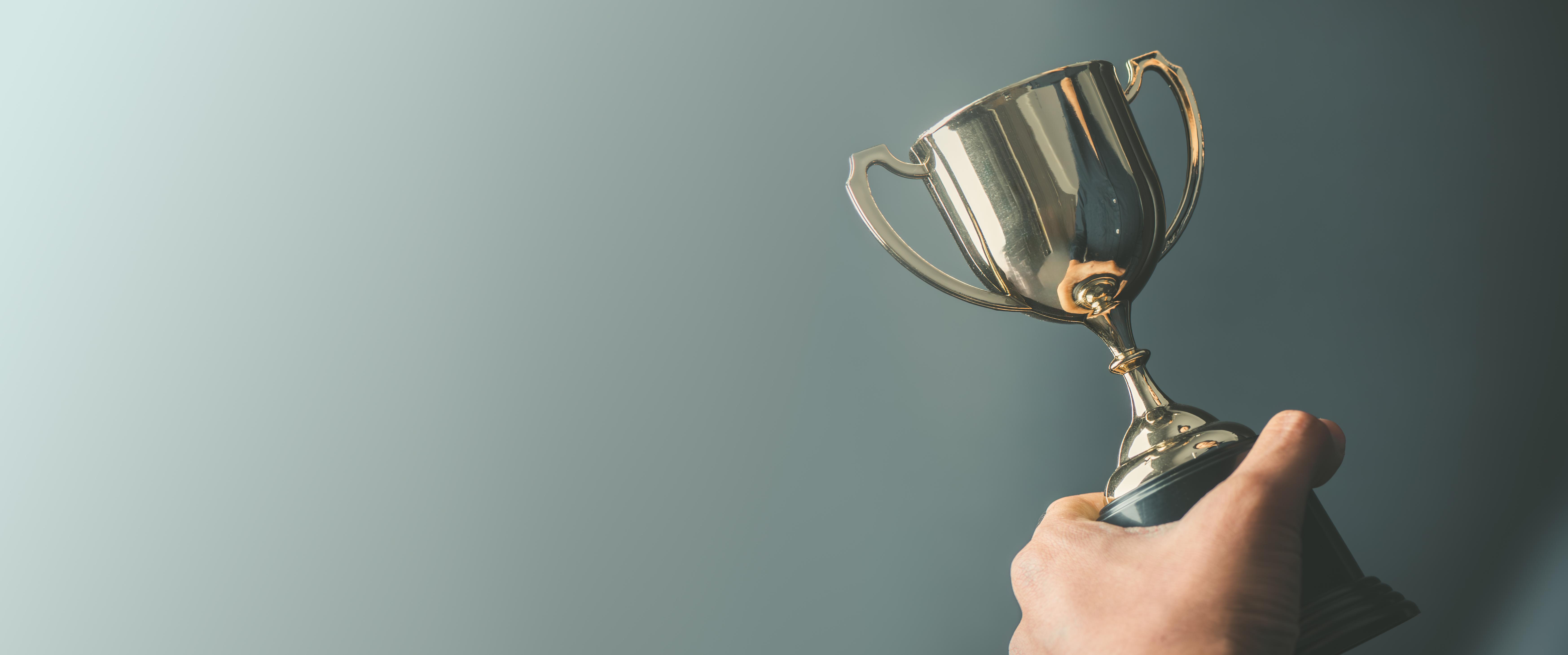 A hand holding a trophy against a grey background.