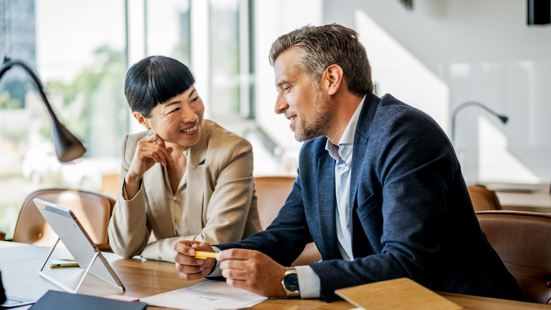 A financial employee and a patient are discussing financial support in a modern office, using a digital tablet and paperwork