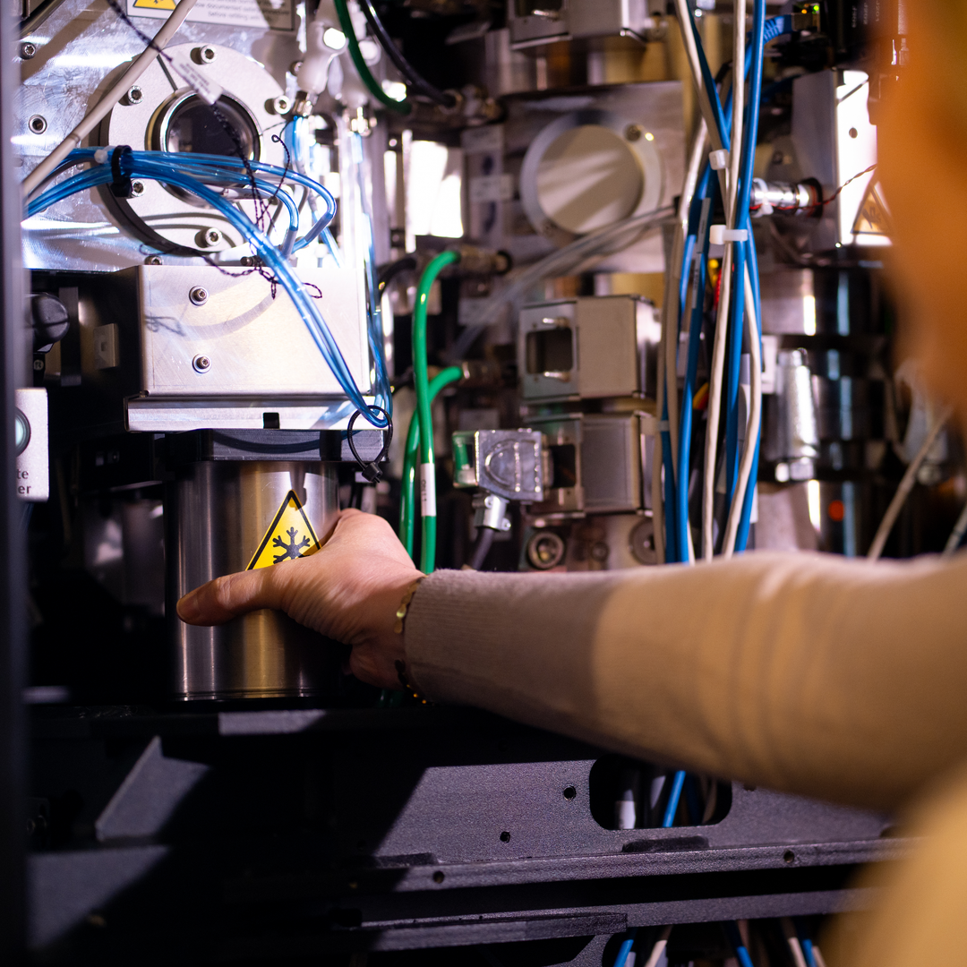 A metal vessel the size of a large mug with a snowflake caution icon on it, is placed inside a large dark machine filled with multi-colored wires