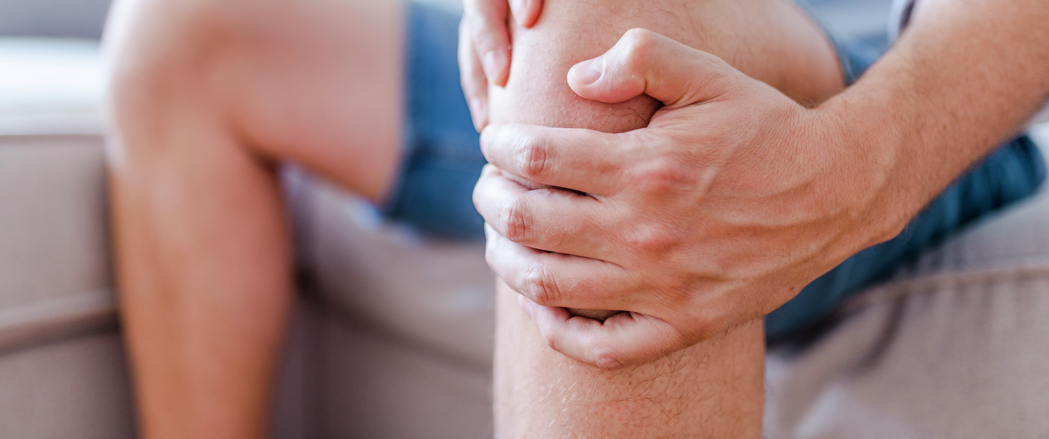 A person sitting on a couch holds their knee in pain
