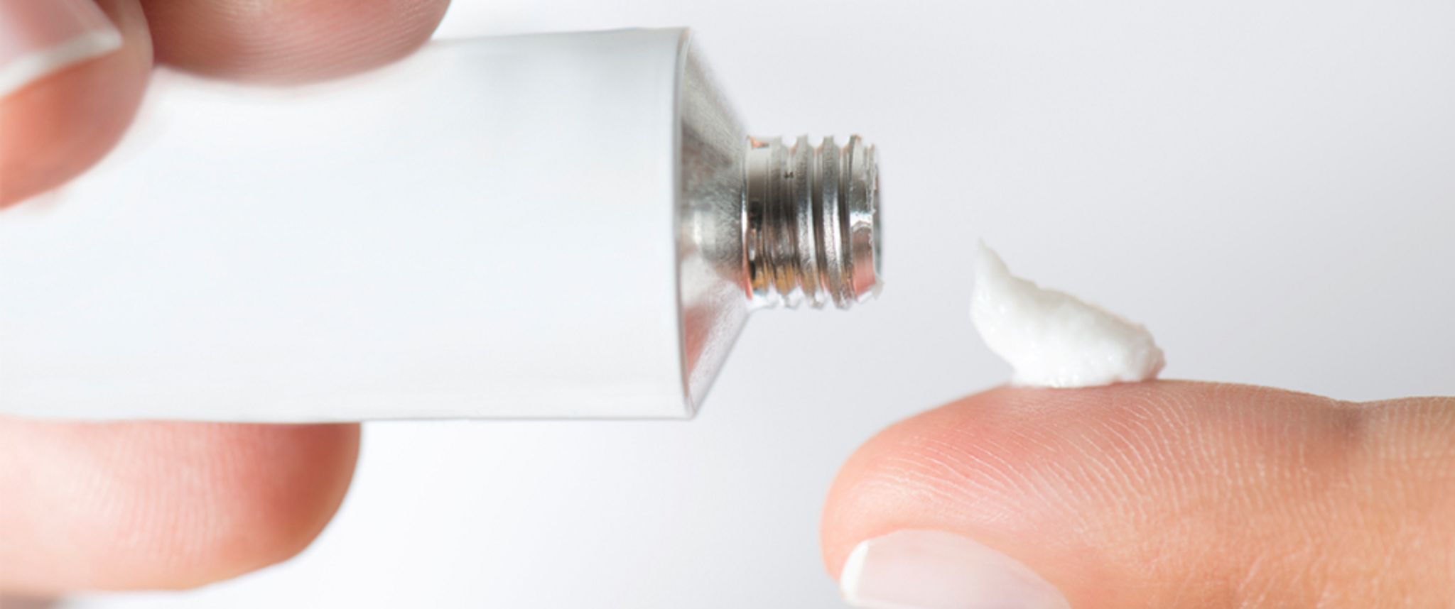 Skin cream being applied to the fingertip from a white tube