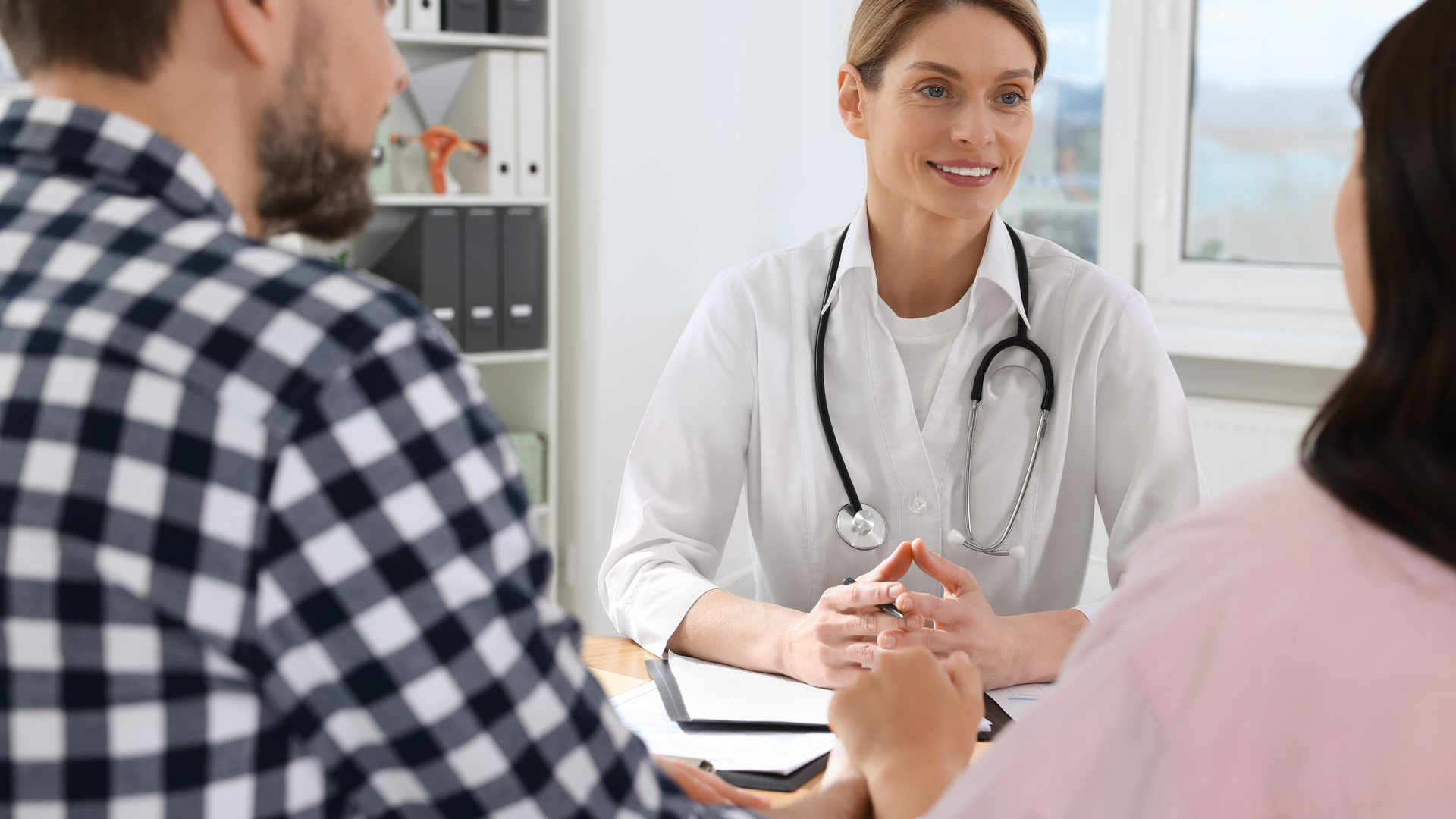 A woman doctor sits behind a desk and talks to a couple