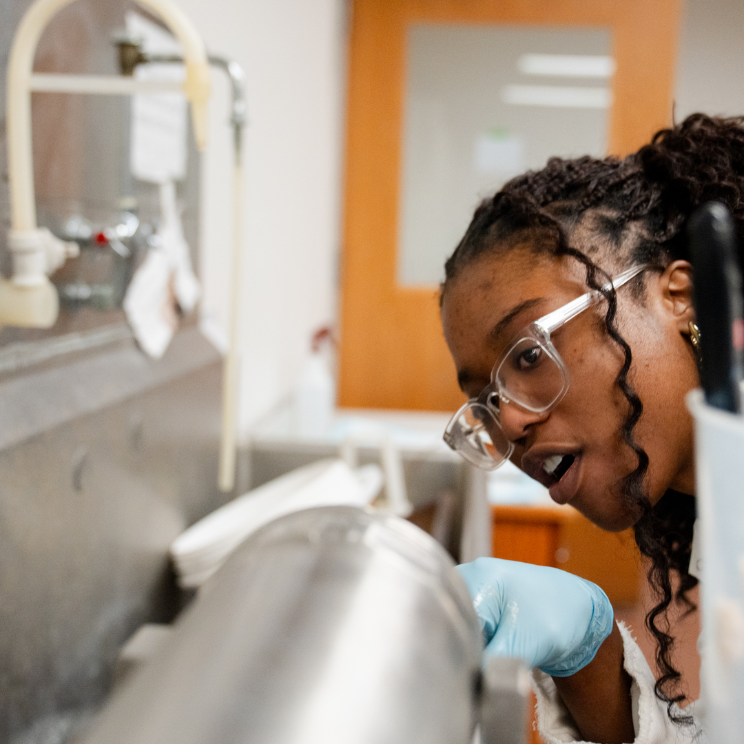 A female scientist looks into a metal apparatus