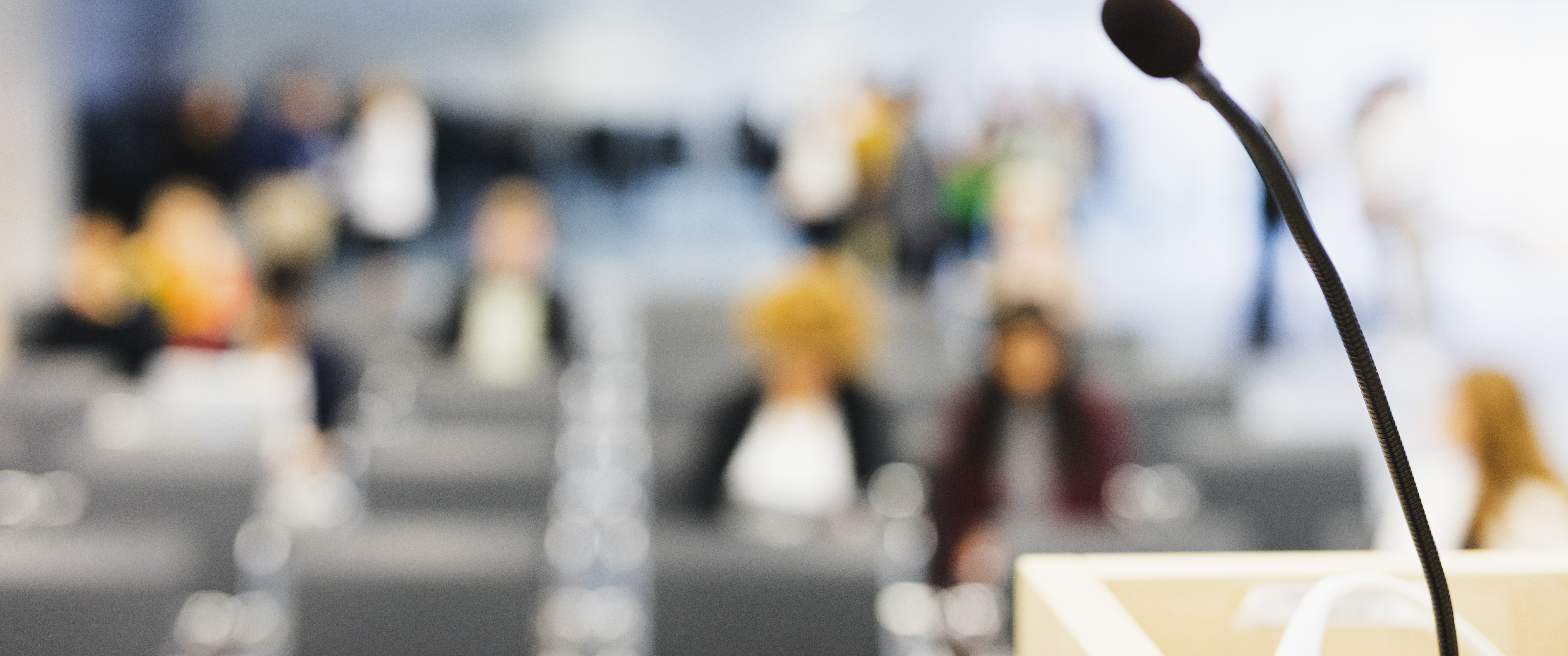 A microphone on a  lectern with a group of people sitting in the background