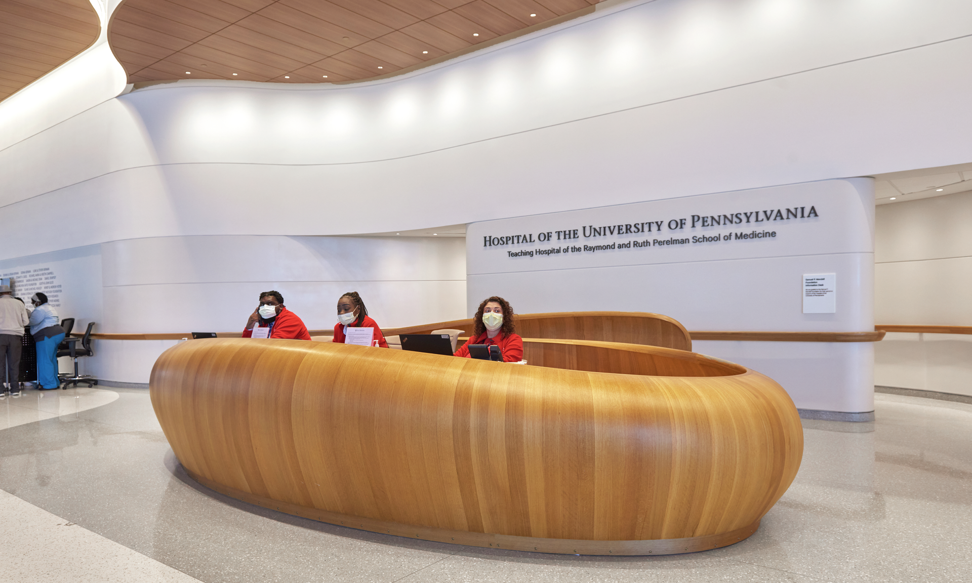 Three staff members in red coats sit behind a large, curved wooden desk