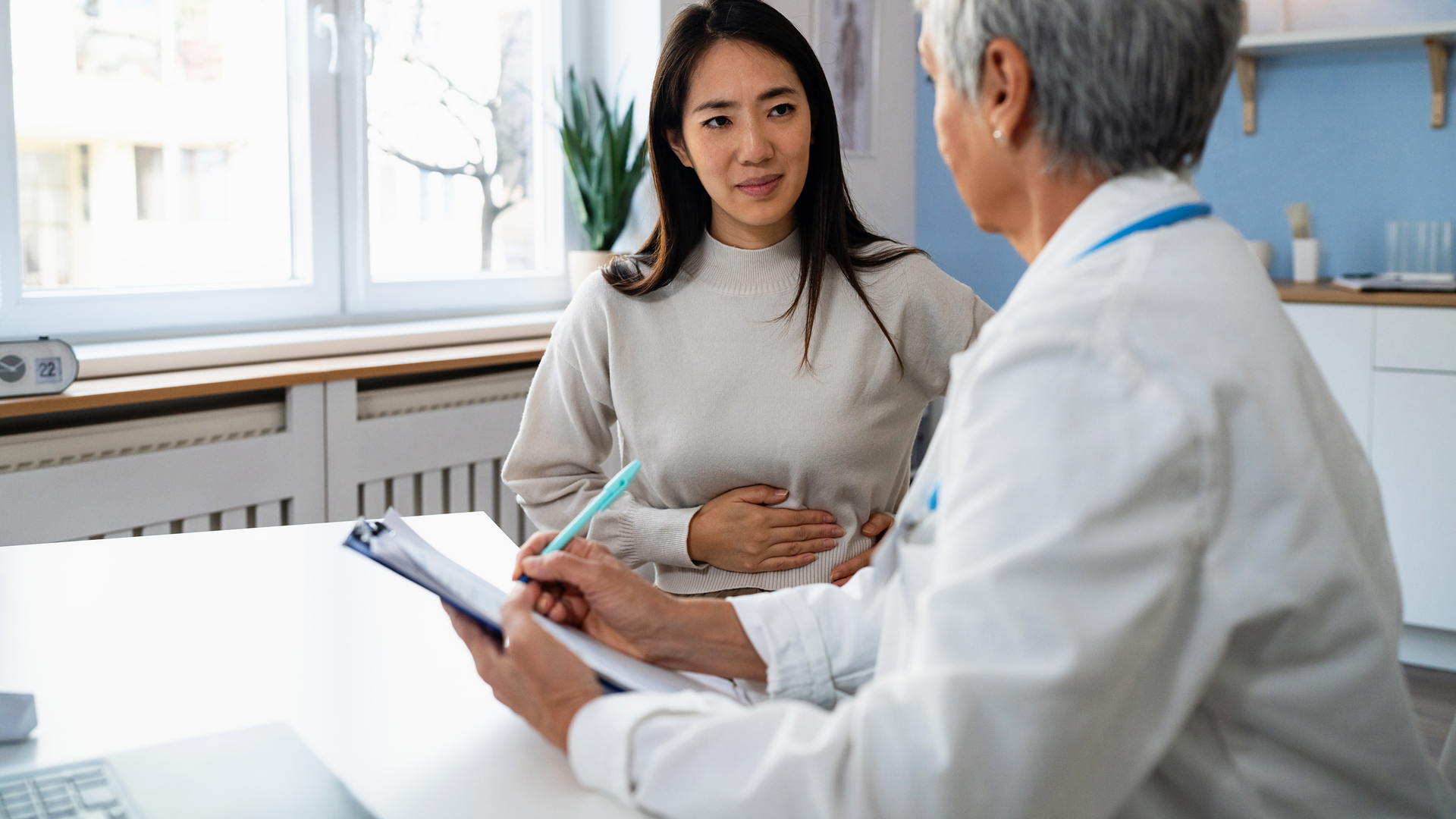 Female patient explaining her stomach ache symptoms to senior female doctor