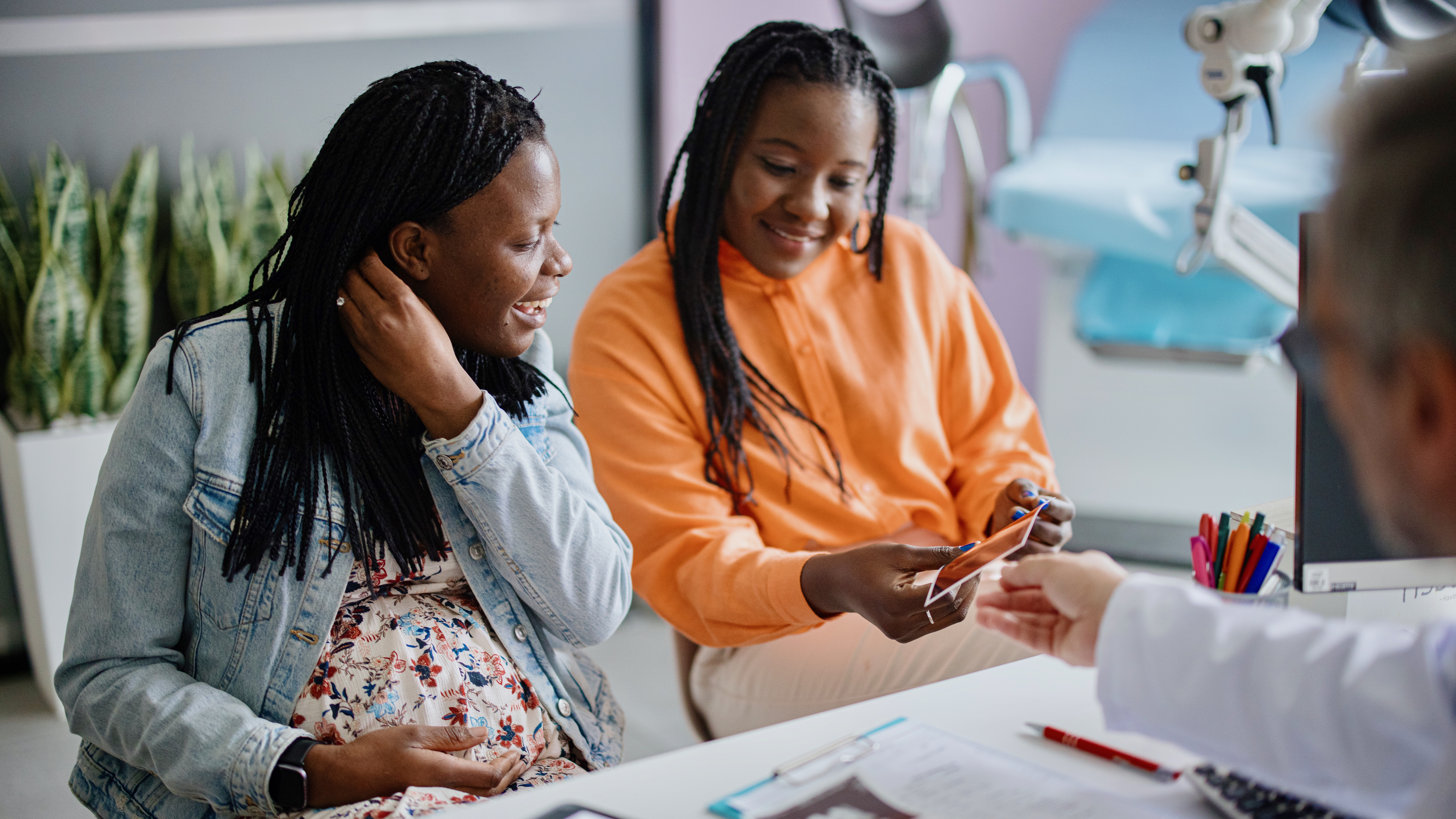 A pregnant woman and her wife smiling as a doctor hands them ultrasound images of their fetus.