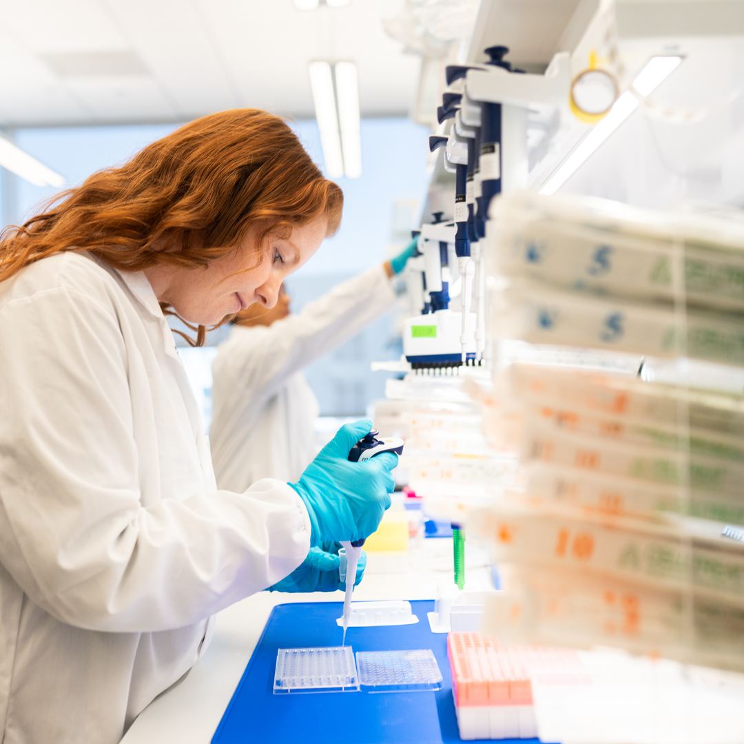 A researcher in a white lab coat uses a pipette at a lab bench